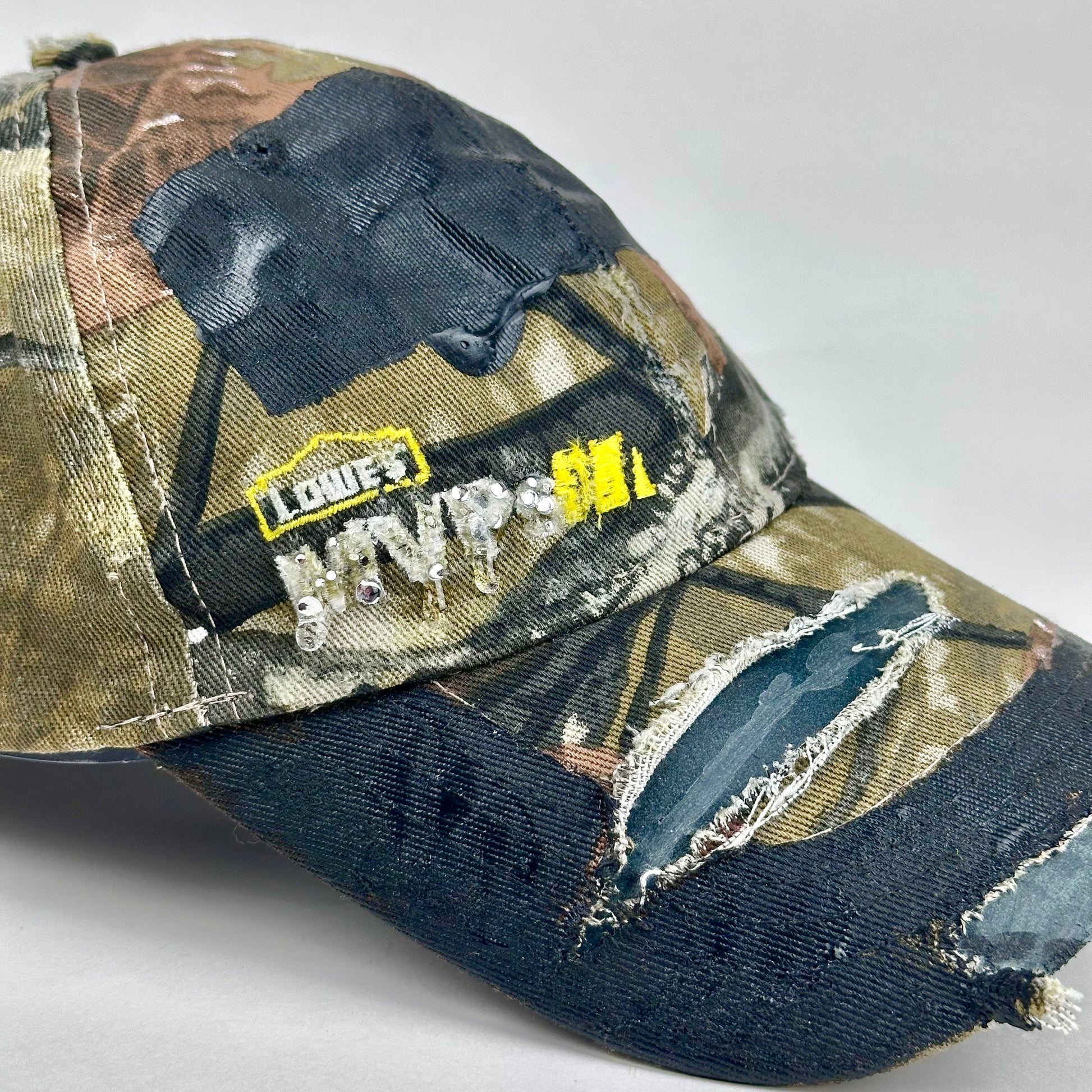 Logo detail on ASTROBOI* x Lowe’s MVP brown RealTree camouflage hat with resin-sealed rhinestone logo, black waxed tattoo print, adjustable strap, custom NYC piece