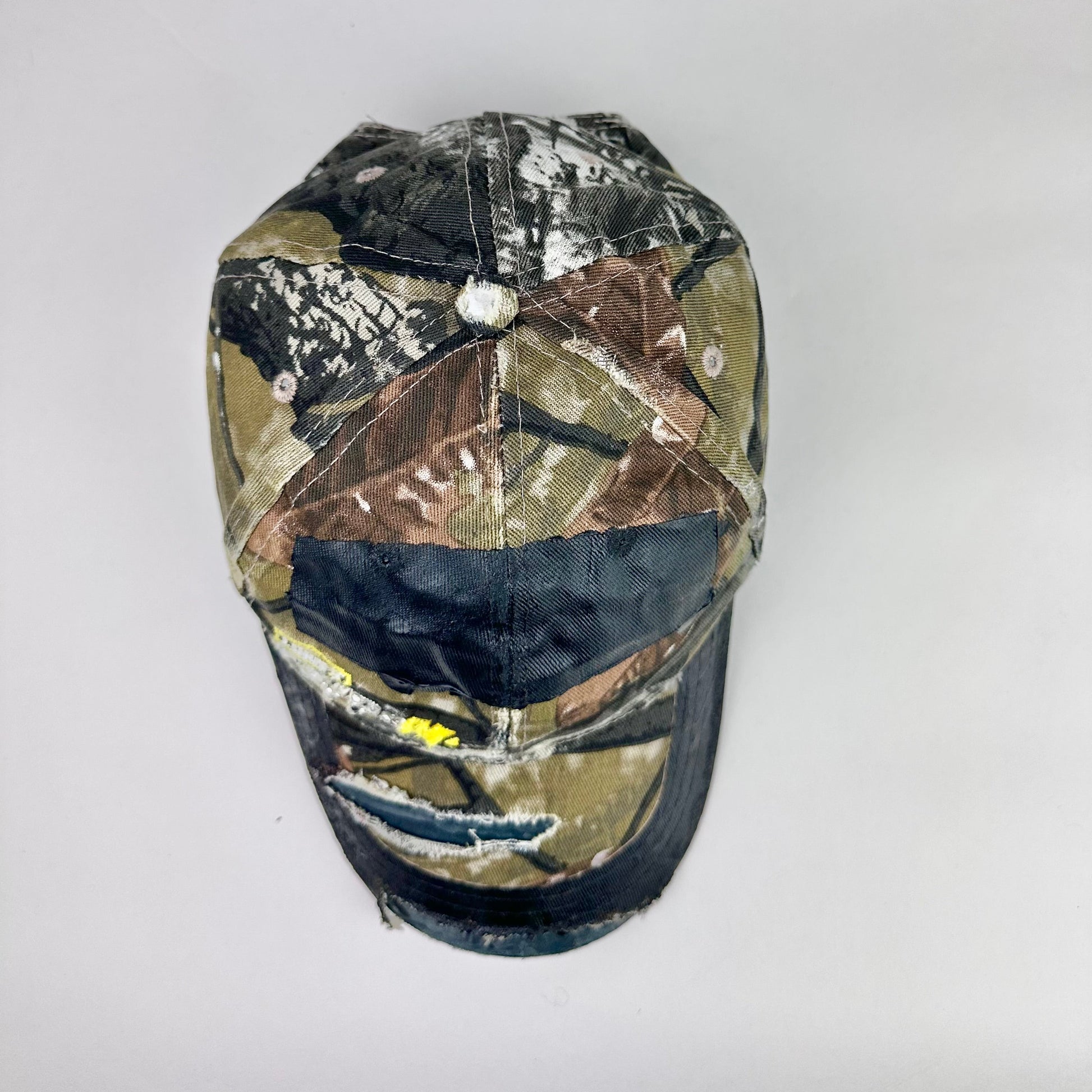 Still life top of ASTROBOI* x Lowe’s MVP brown RealTree camouflage hat with resin-sealed rhinestone logo, black waxed tattoo print, adjustable strap, custom NYC piece