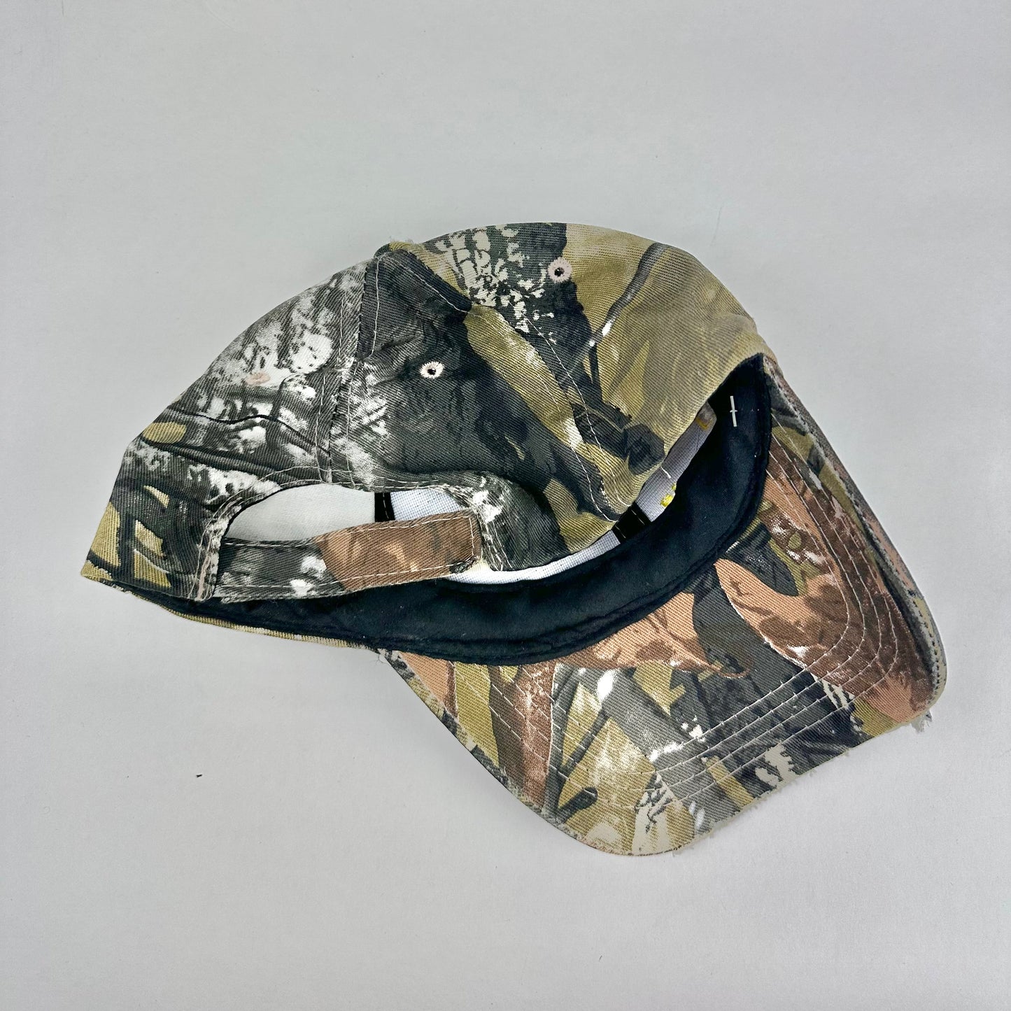 Product shot back angle of ASTROBOI* x Lowe’s MVP brown RealTree camouflage hat with resin-sealed rhinestone logo, black waxed tattoo print, adjustable strap, custom NYC piece