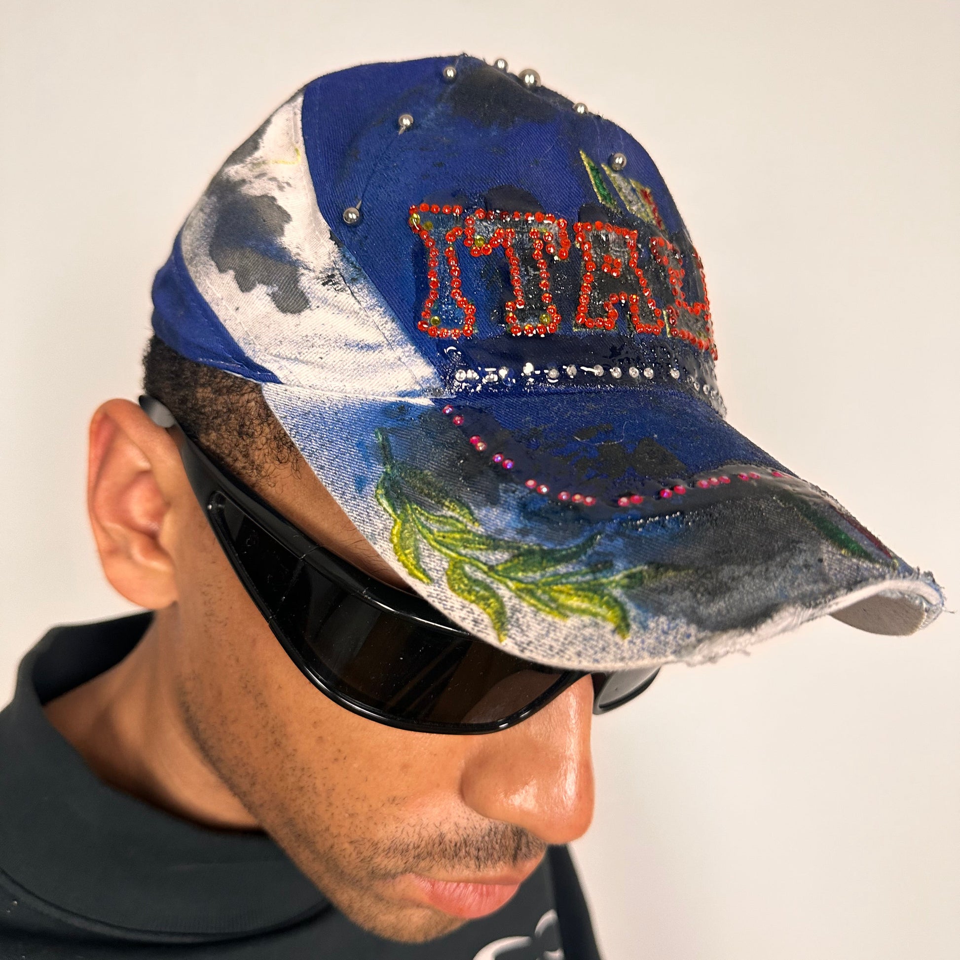 Front right of Upcycled blue and white ASTROBOI* ‘ITALIA’ hat with rhinestones, resin, custom paint, and stainless steel piercings, handcrafted in NYC.