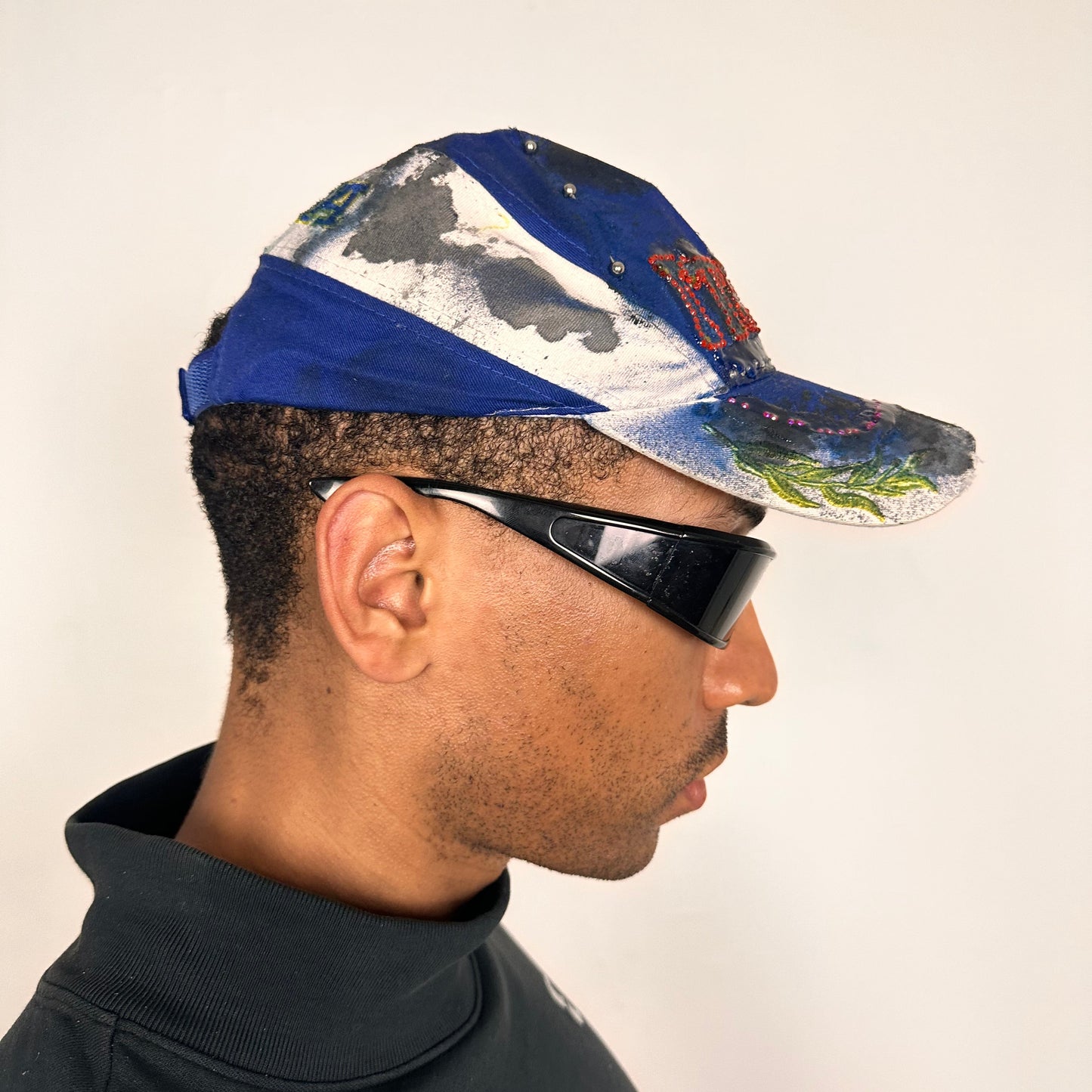 Right of Upcycled blue and white ASTROBOI* ‘ITALIA’ hat with rhinestones, resin, custom paint, and stainless steel piercings, handcrafted in NYC.