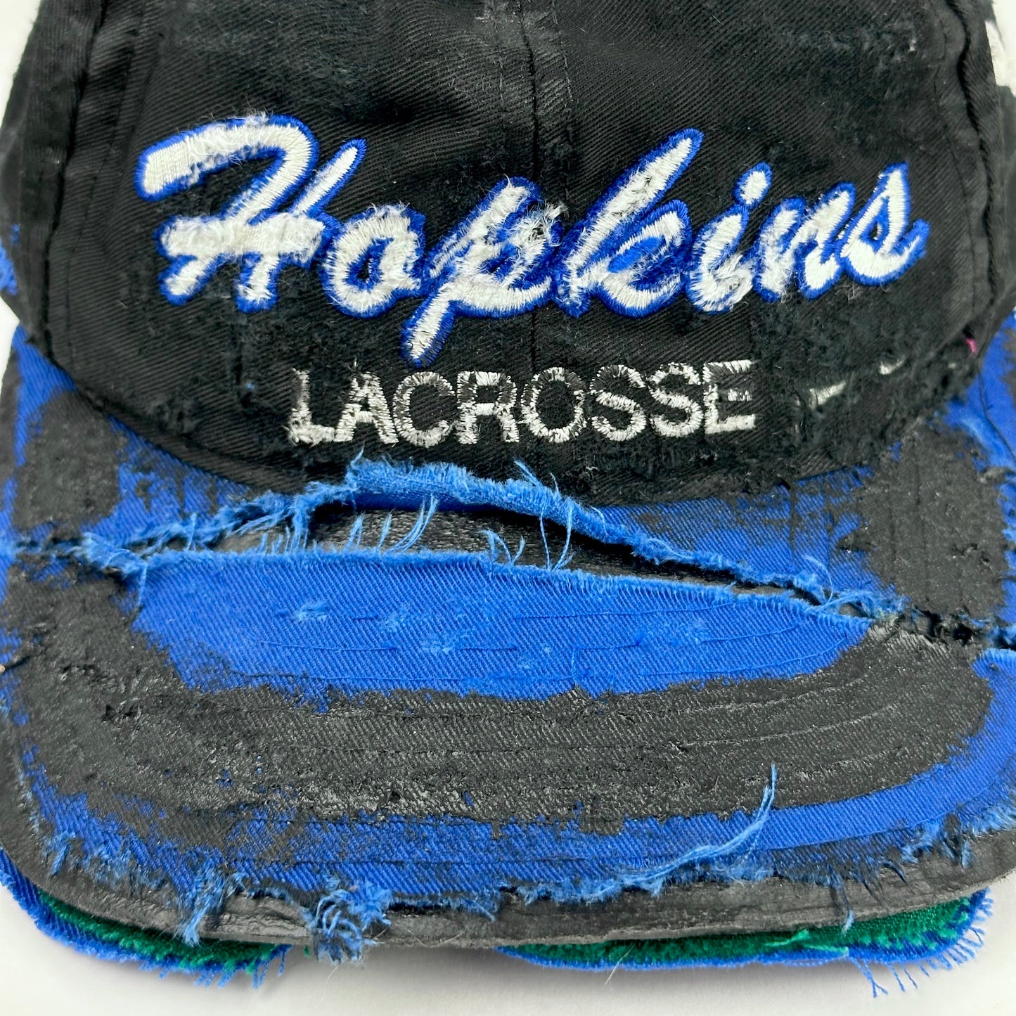 Front close up of Black distressed ASTROBOI* Hopkins Lacrosse cap with blue embroidery and custom black paint treatment, snapback style, handcrafted in NYC.