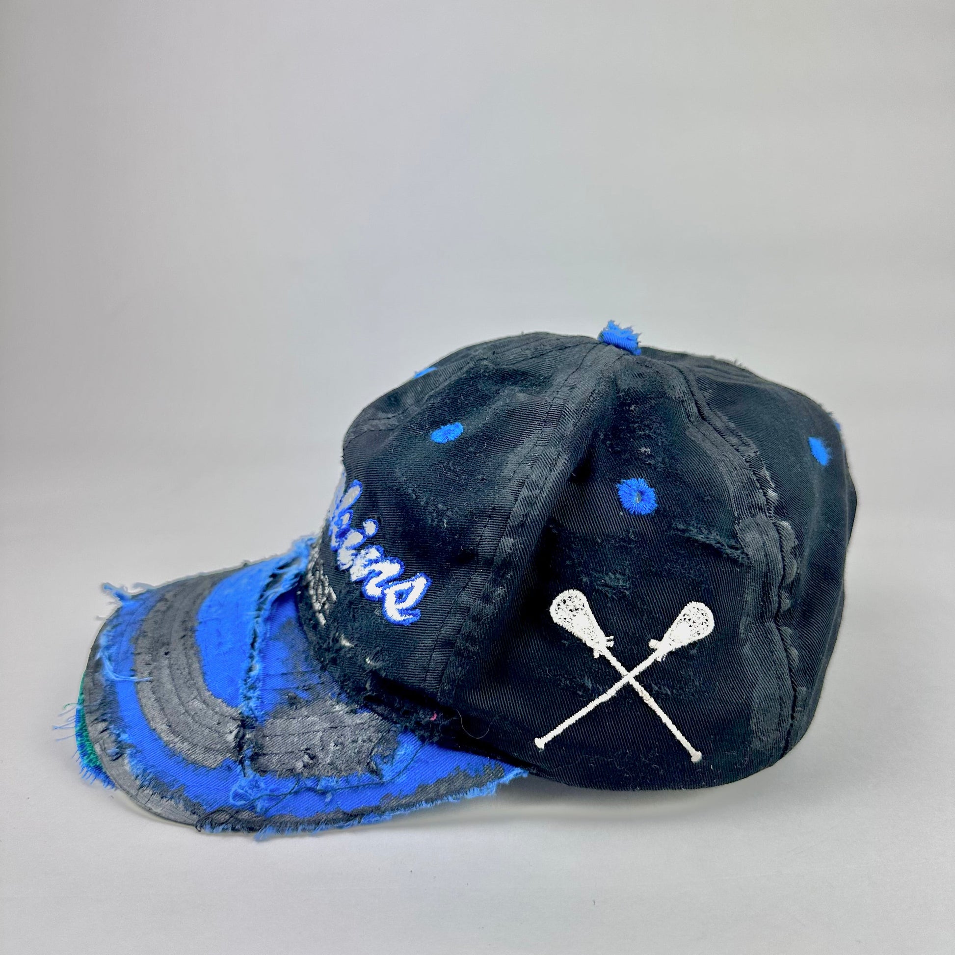 White embroidered lacrosse sticks on the side of black and blue baseball hat