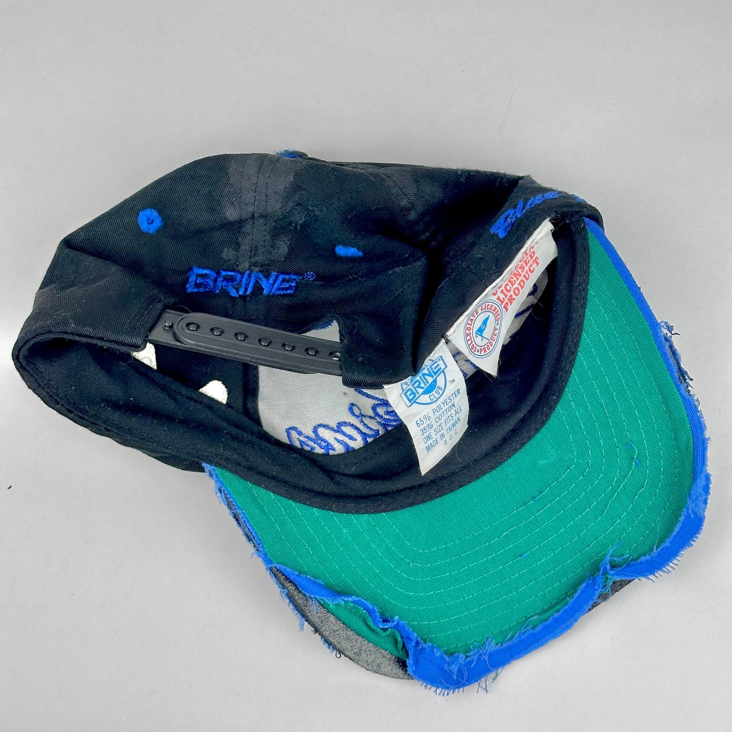 Snapback closure detail on Baseball cap with green front and black back on a light gray background