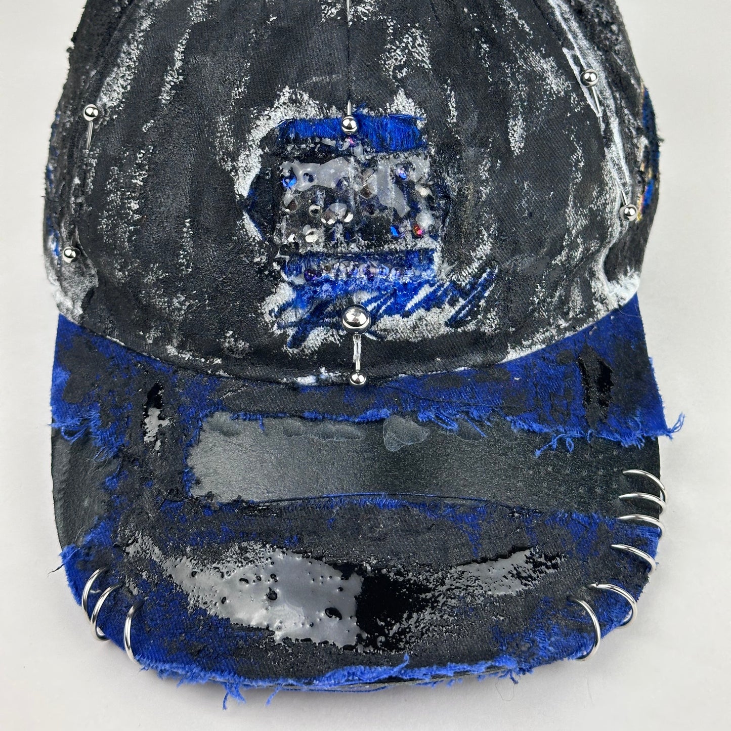 Front detail shot on Blue and white ASTROBOI* NAPA hat with rhinestone-covered logo sealed in clear resin, stainless steel piercings, and a deconstructed visor, handcrafted in NYC.