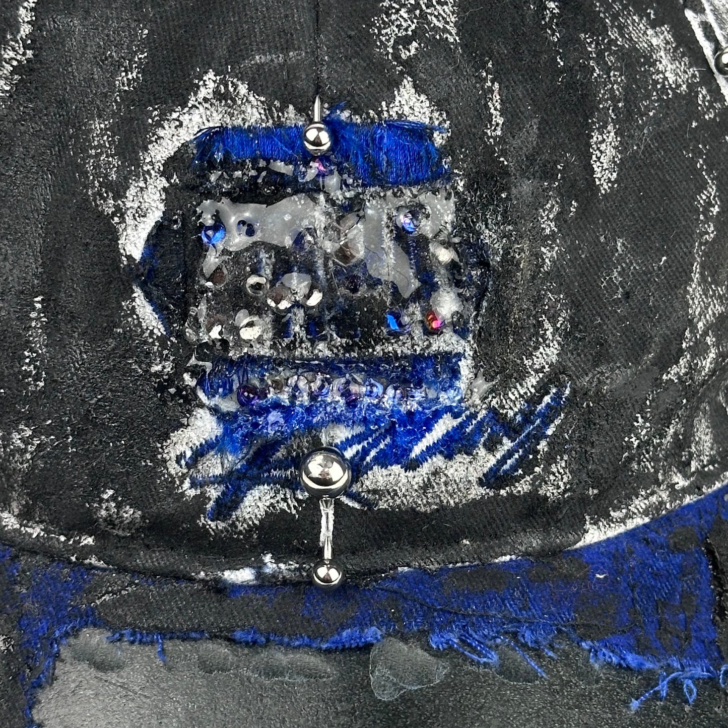 Logo detail on Blue and white ASTROBOI* NAPA hat with rhinestone-covered logo sealed in clear resin, stainless steel piercings, and a deconstructed visor, handcrafted in NYC.