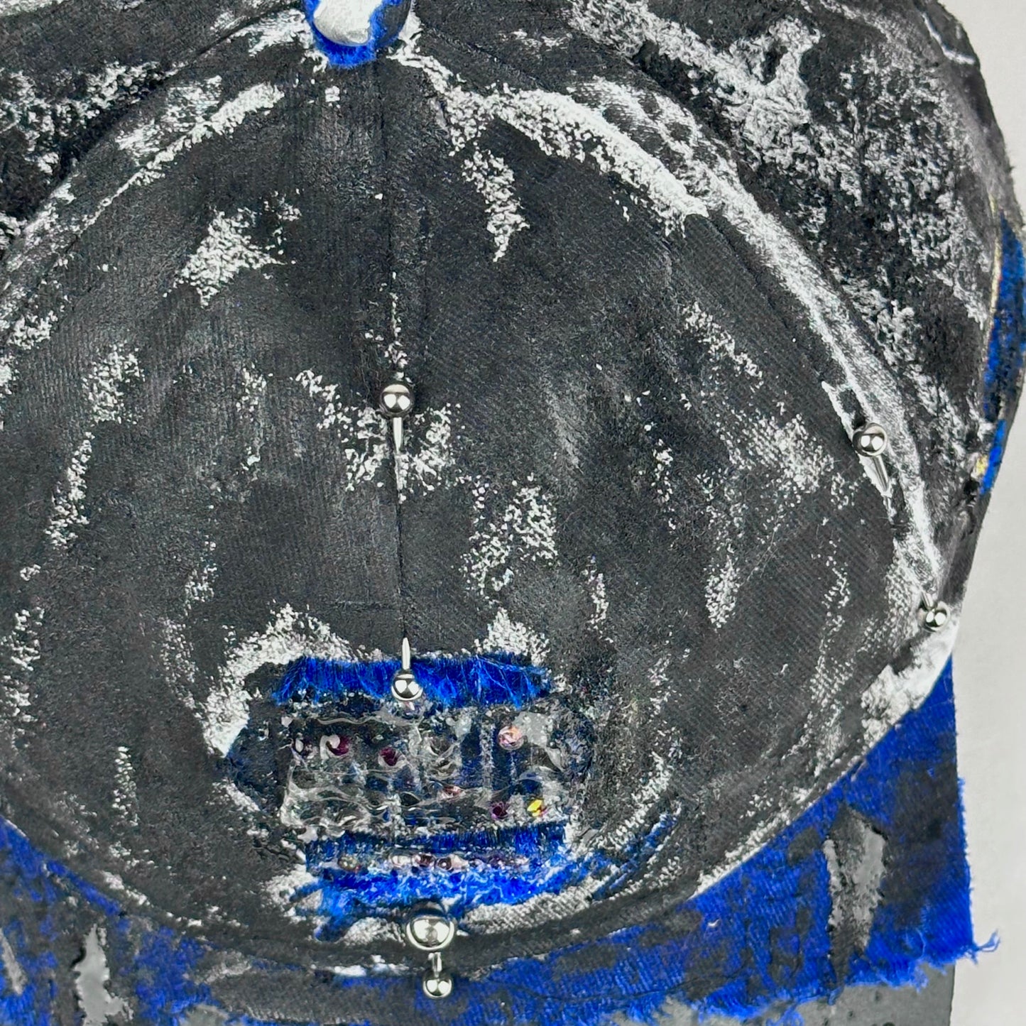 Top piercing detail on Blue and white ASTROBOI* NAPA hat with rhinestone-covered logo sealed in clear resin, stainless steel piercings, and a deconstructed visor, handcrafted in NYC.