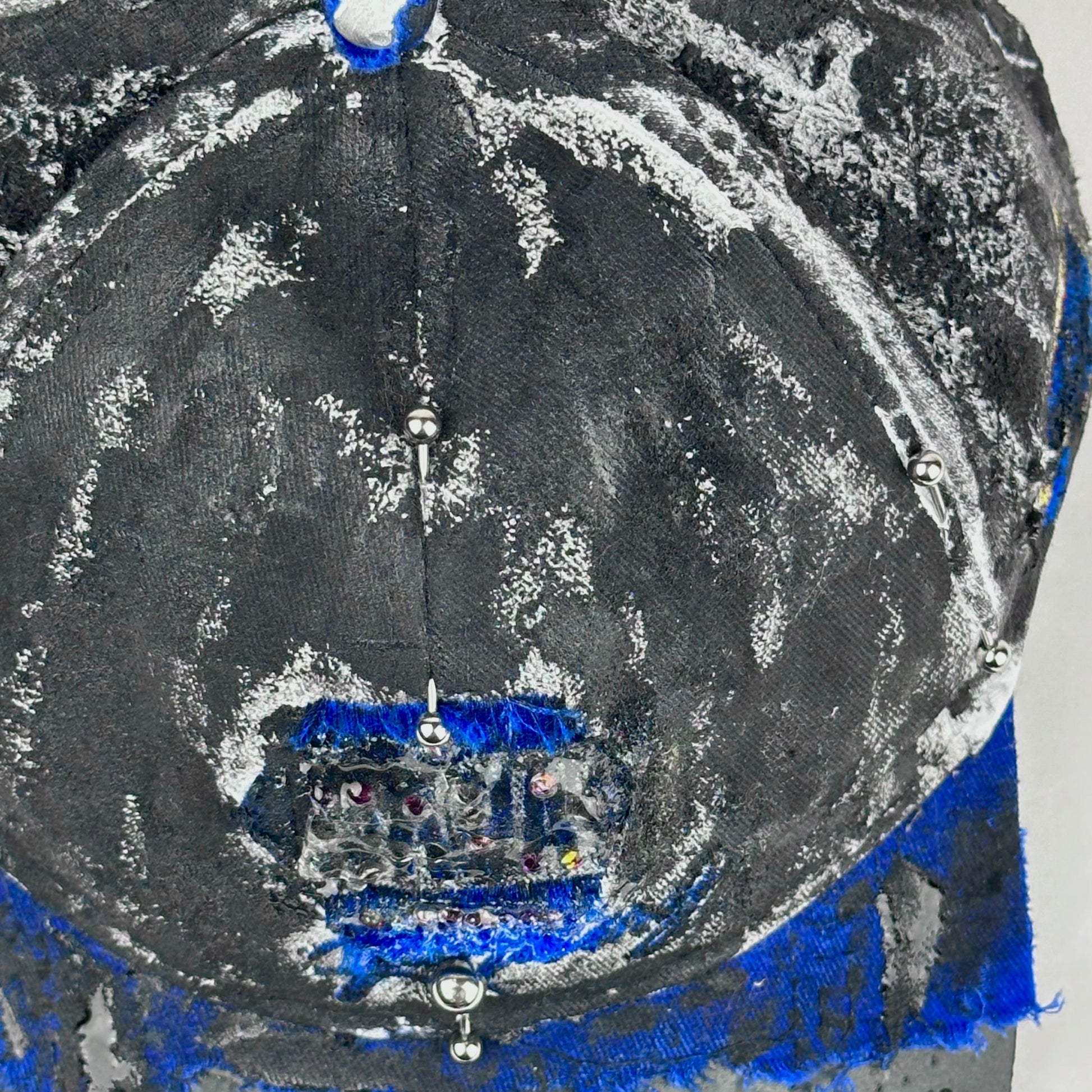 Top piercing detail on Blue and white ASTROBOI* NAPA hat with rhinestone-covered logo sealed in clear resin, stainless steel piercings, and a deconstructed visor, handcrafted in NYC.