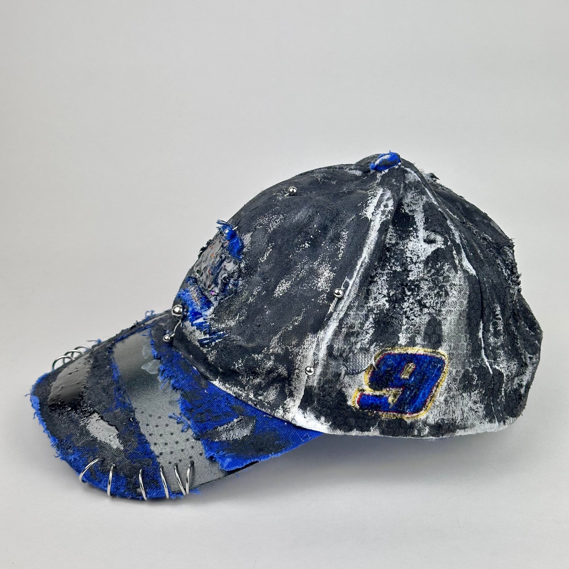 Left side of Blue and white ASTROBOI* NAPA hat with rhinestone-covered logo sealed in clear resin, stainless steel piercings, and a deconstructed visor, handcrafted in NYC.