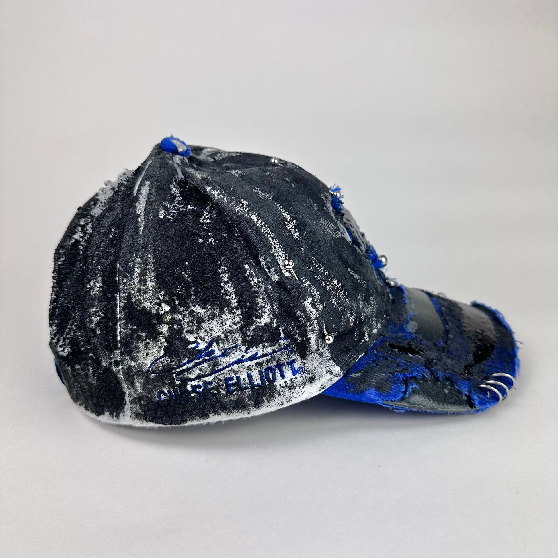 Left side of Blue and white ASTROBOI* NAPA hat with rhinestone-covered logo sealed in clear resin, stainless steel piercings, and a deconstructed visor, handcrafted in NYC.