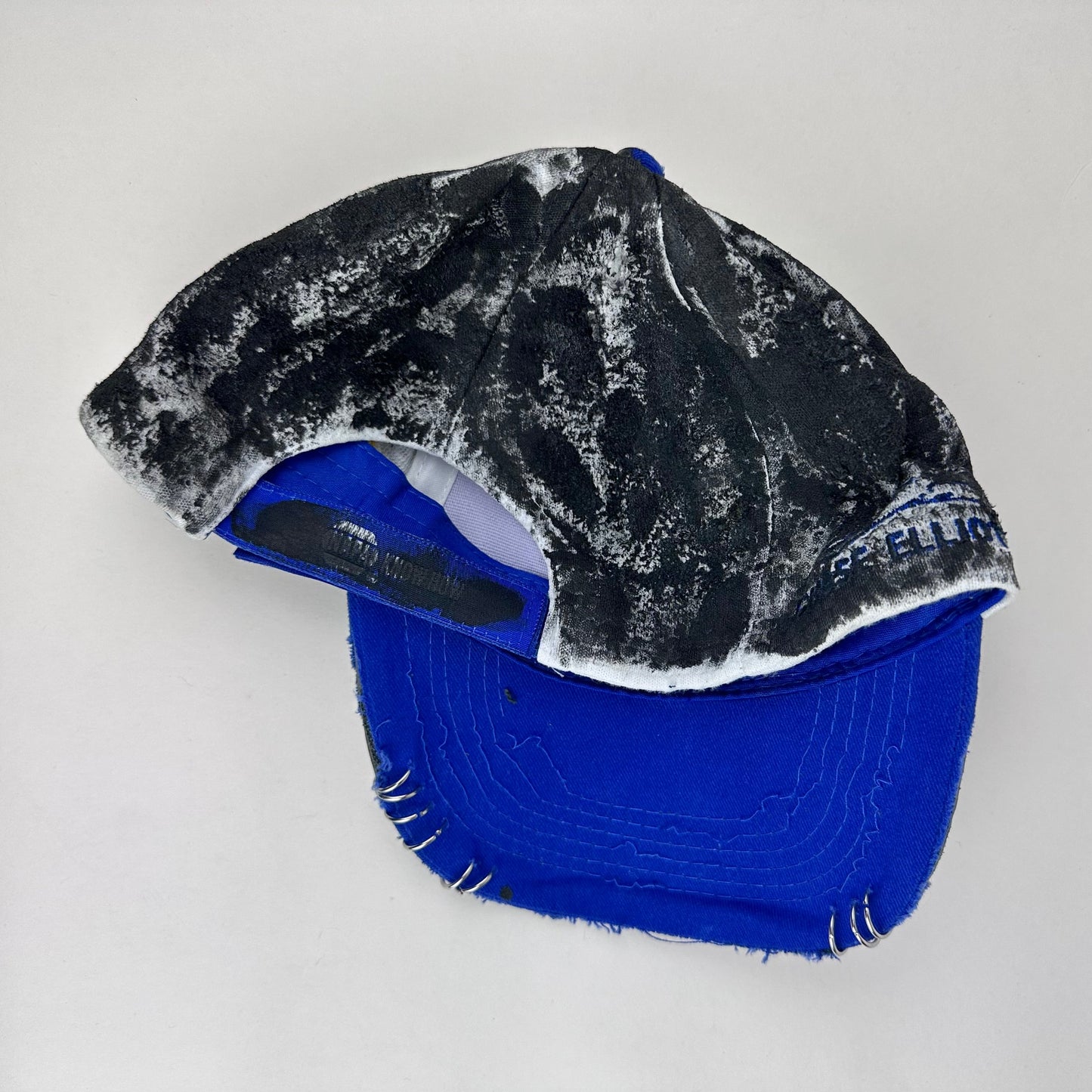 Back of Blue and white ASTROBOI* NAPA hat with rhinestone-covered logo sealed in clear resin, stainless steel piercings, and a deconstructed visor, handcrafted in NYC.