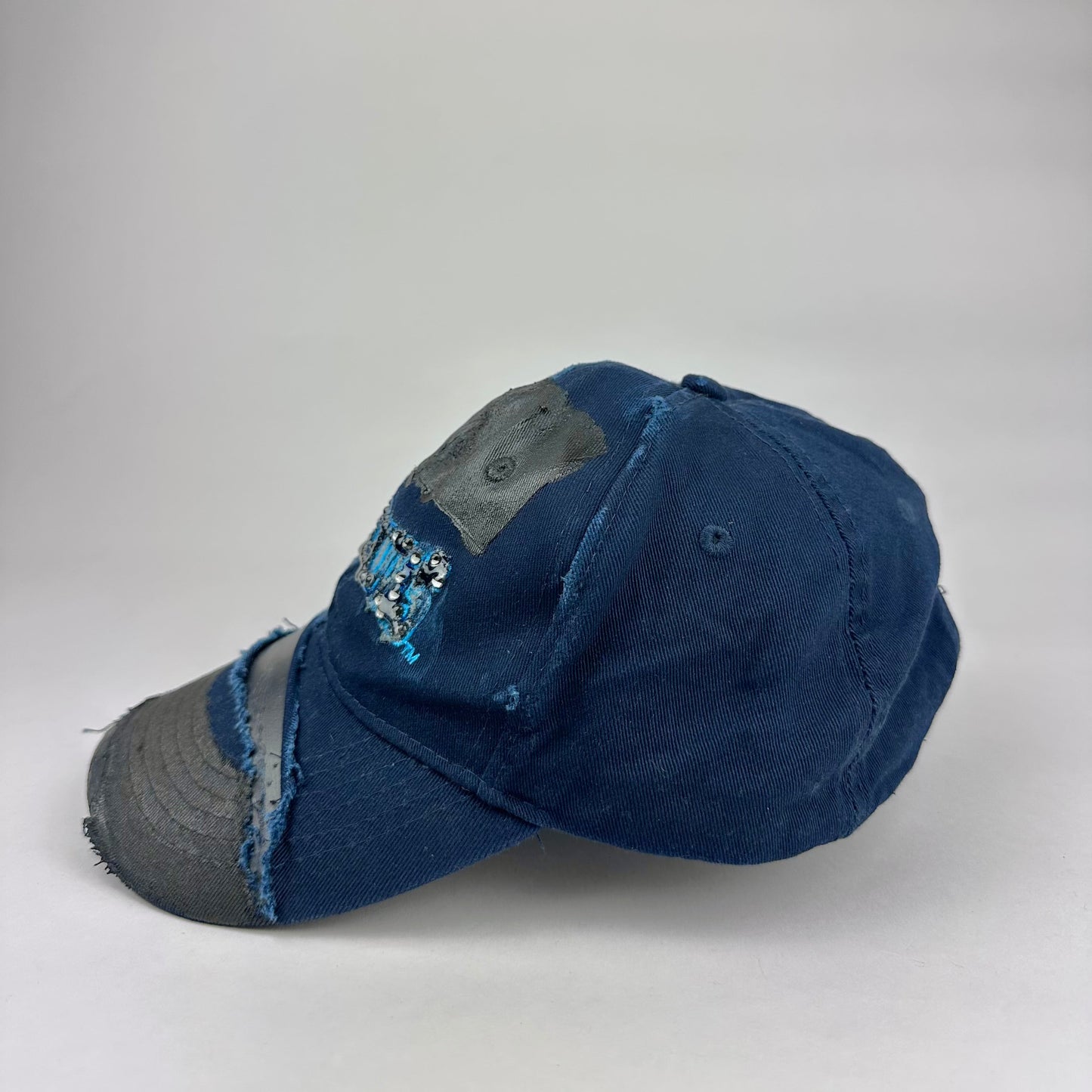 Left product shot of ASTROBOI* x Renegades navy distressed hat with resin-sealed rhinestones and tattoo-style paint details. One-of-one custom piece made in NYC.