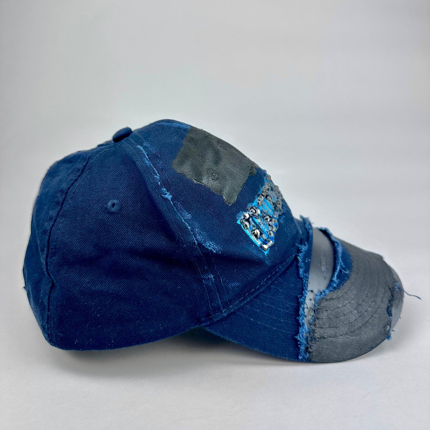 Right side product shot of ASTROBOI* x Renegades navy distressed hat with resin-sealed rhinestones and tattoo-style paint details. One-of-one custom piece made in NYC.