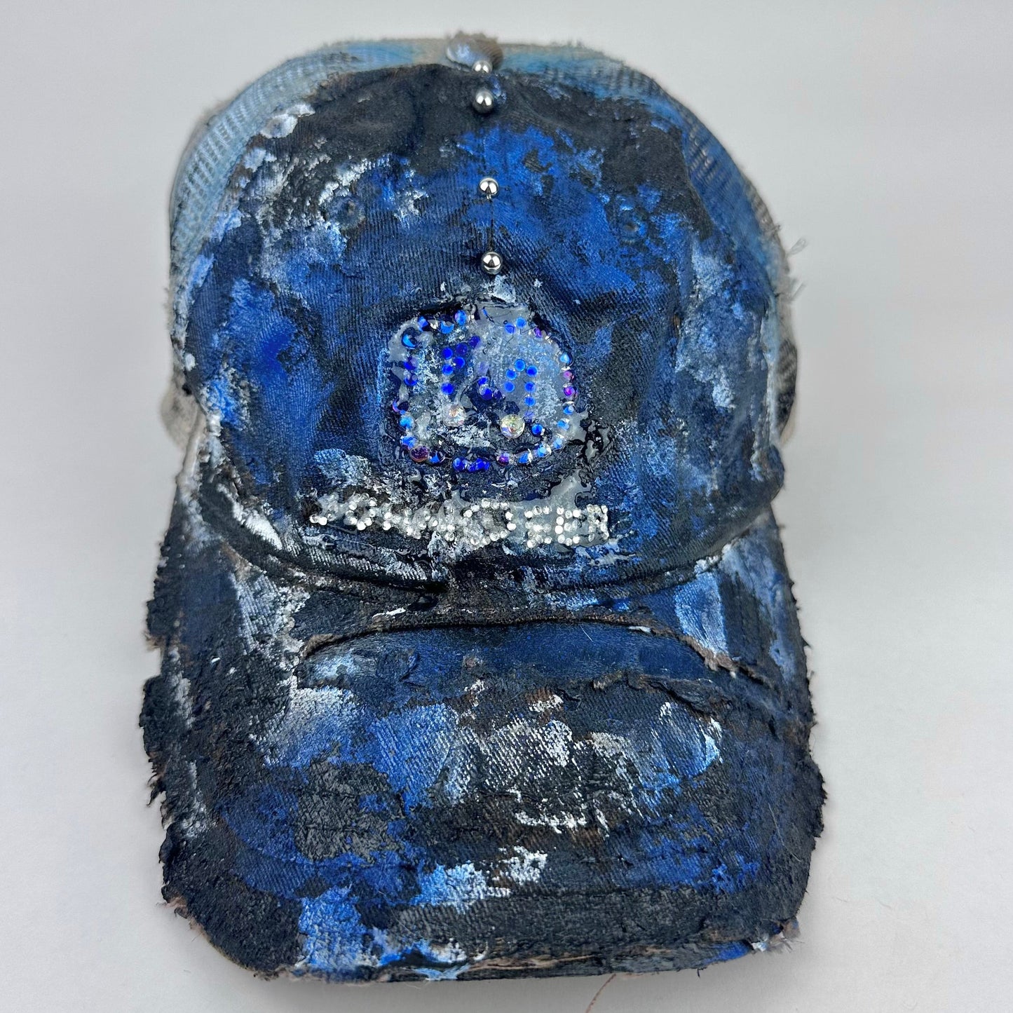 Frontal project shot image of ASTROBOI* x John Deere black and blue distressed trucker hat with rhinestone resin logo and stainless steel piercings.