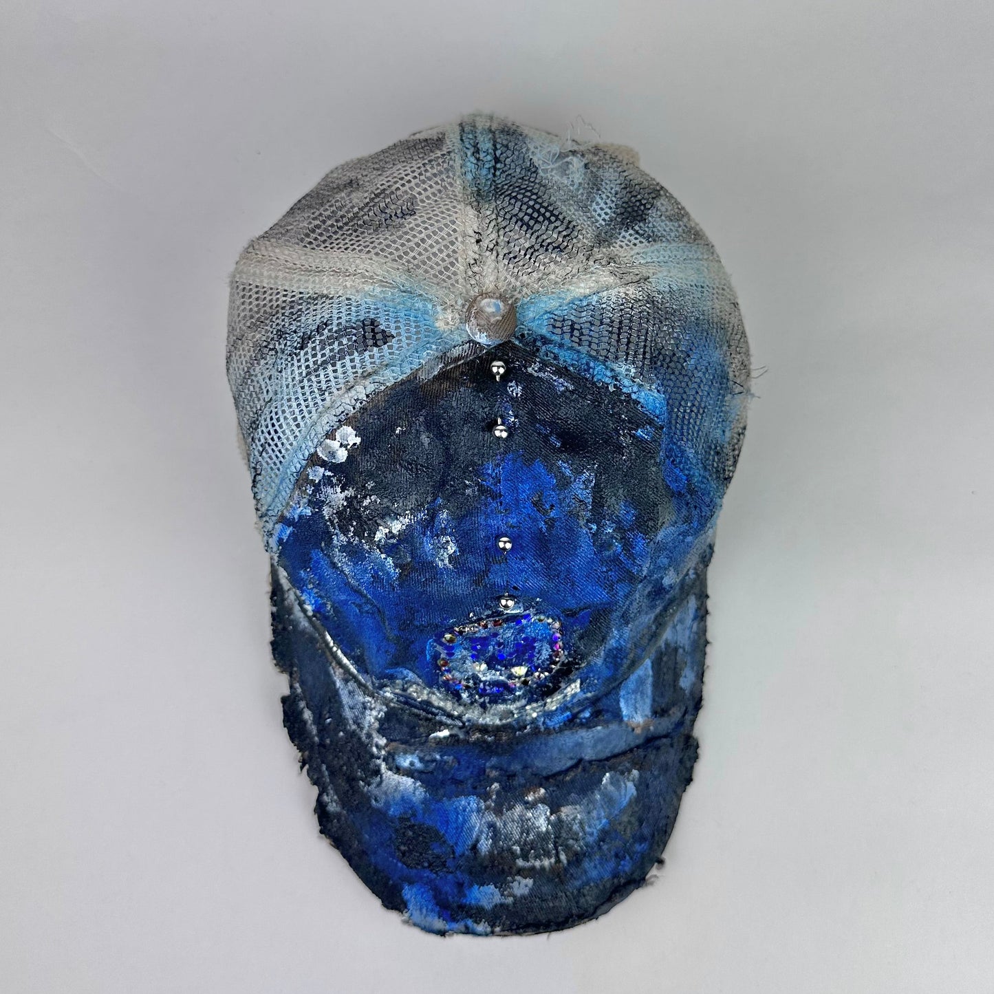 Top angle of ASTROBOI* x John Deere black and blue distressed trucker hat with rhinestone resin logo and stainless steel piercings.