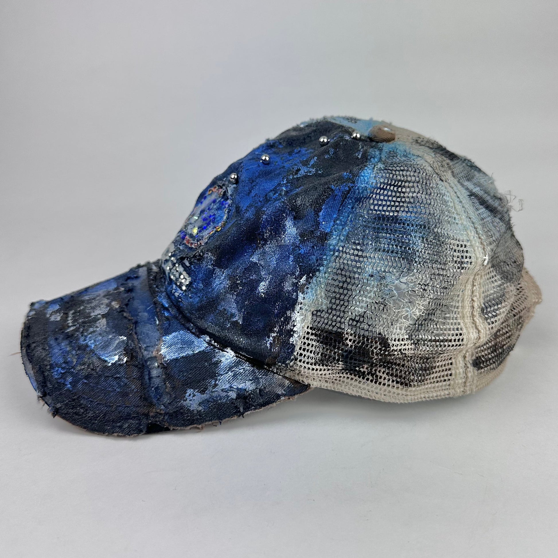 Left side of ASTROBOI* x John Deere black and blue distressed trucker hat with rhinestone resin logo and stainless steel piercings.