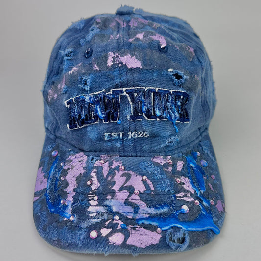 Front image of ASTROBOI* 'Twilight Haze' distressed blue resin hat with New York logo, lavender metallic paint treatment, oozing resin effect, and matching lavender rhinestone embellishments, handmade in NYC.