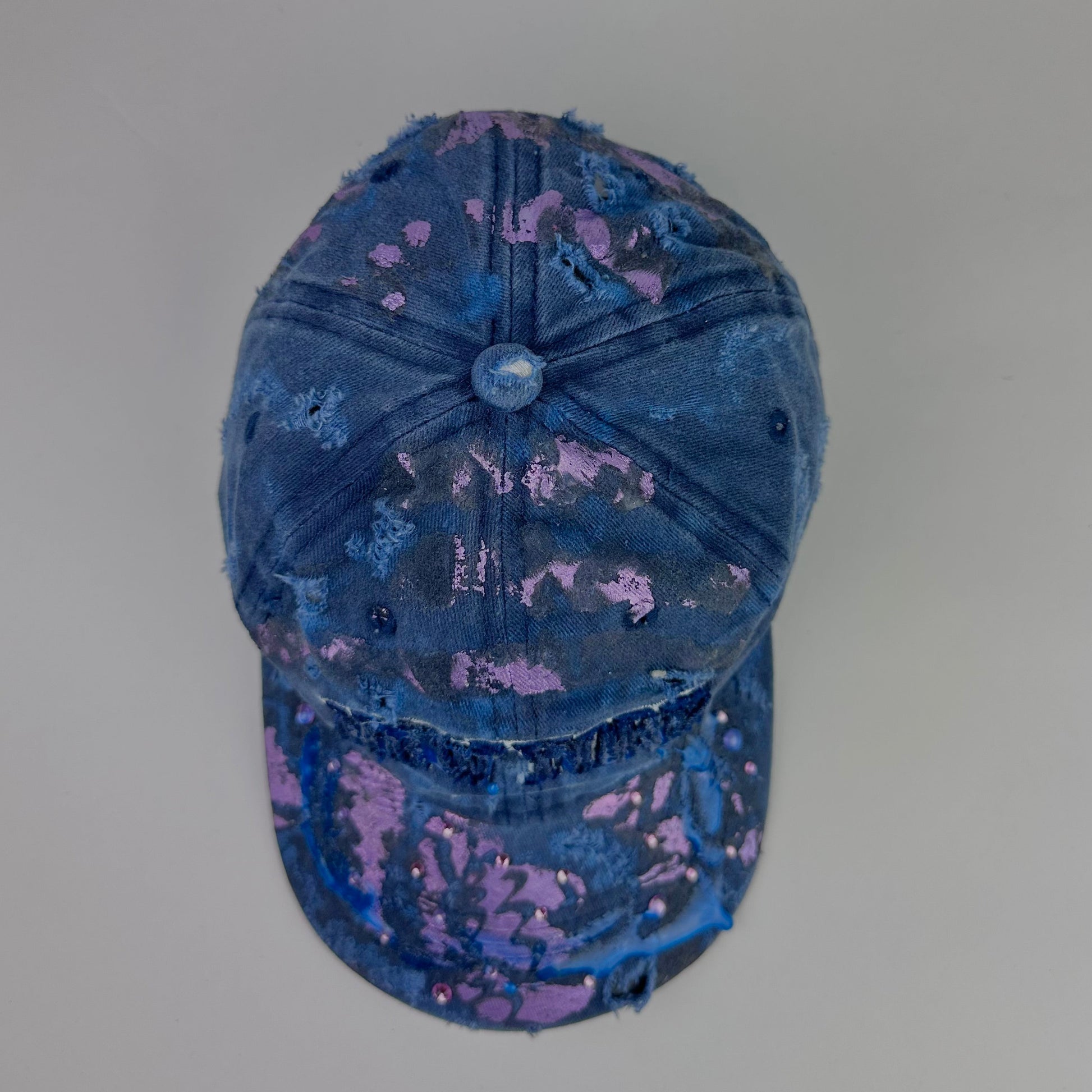 Top of ASTROBOI* 'Twilight Haze' distressed blue resin hat with New York logo, lavender metallic paint treatment, oozing resin effect, and matching lavender rhinestone embellishments, handmade in NYC.