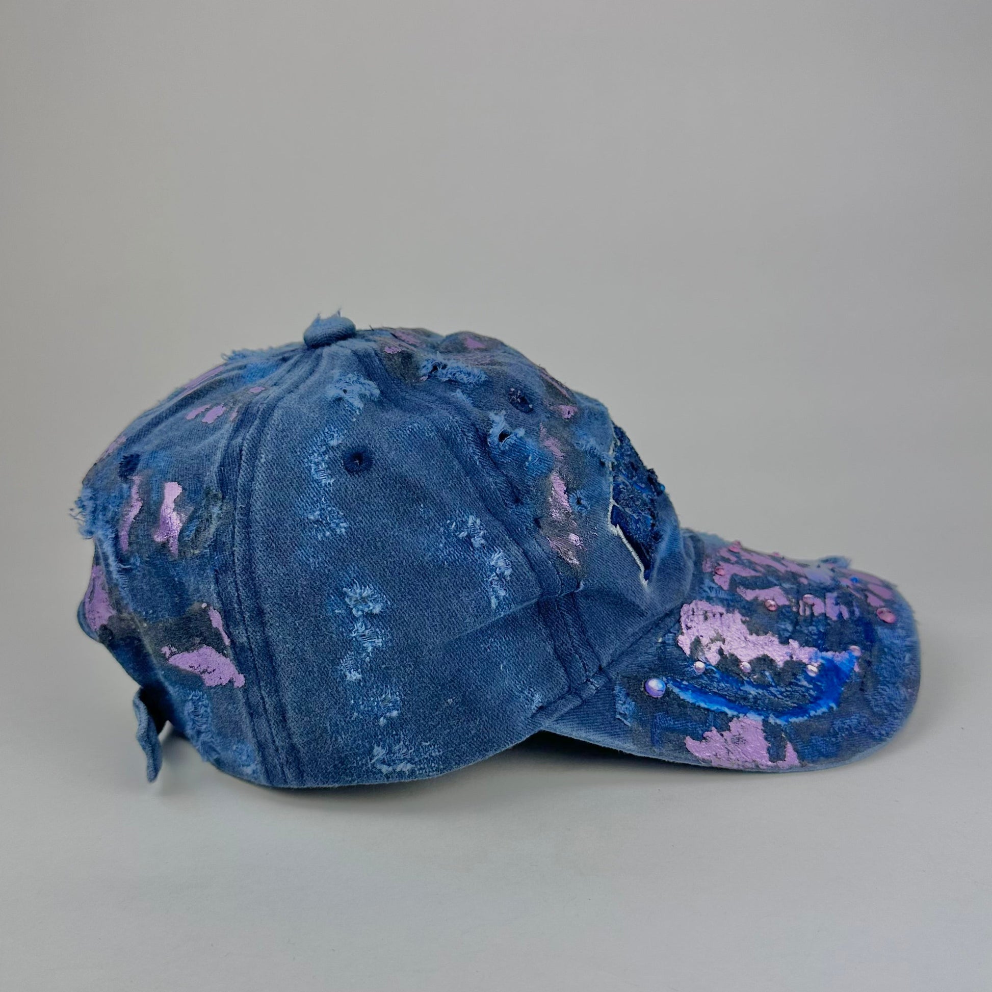 Right side of ASTROBOI* 'Twilight Haze' distressed blue resin hat with New York logo, lavender metallic paint treatment, oozing resin effect, and matching lavender rhinestone embellishments, handmade in NYC.