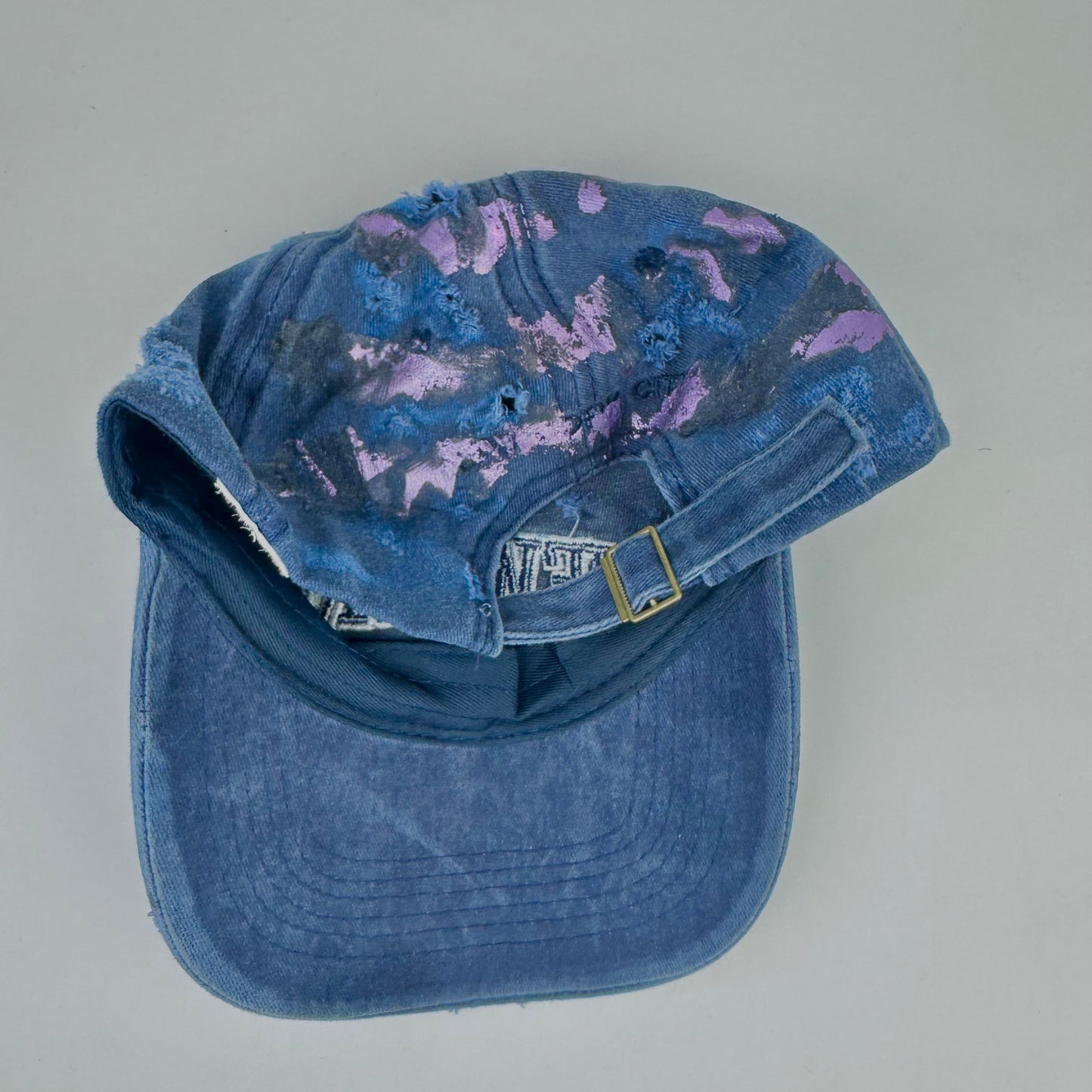 Back of ASTROBOI* 'Twilight Haze' distressed blue resin hat with New York logo, lavender metallic paint treatment, oozing resin effect, and matching lavender rhinestone embellishments, handmade in NYC.