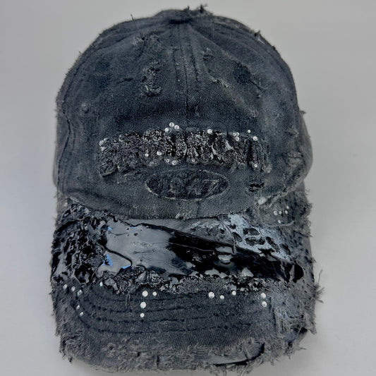 Front of ASTROBOI* 'Tar Diamonds' black distressed resin hat with clear resin Brooklyn embroidery, white paint highlights, black resin visor, and silver rhinestone detailing on logo and brim, crafted in NYC.