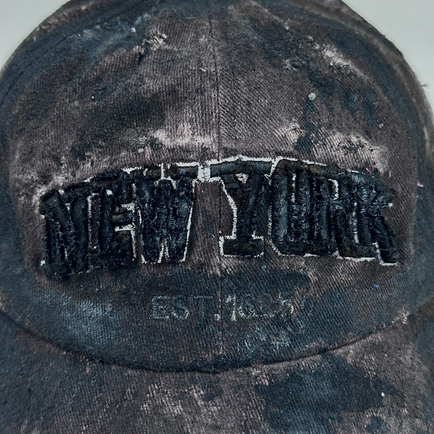 Logo detail on ASTROBOI* New York brown and black distressed half-visor hat with bold logo, black paint accents, and deconstructed grunge design. Handmade in NYC.