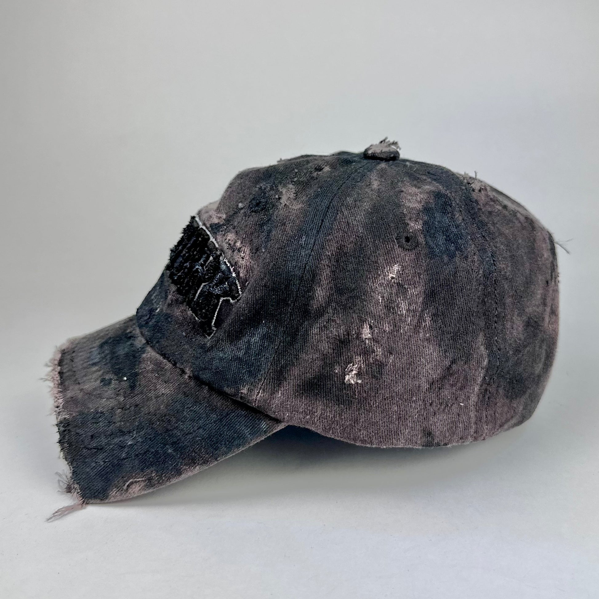 Left side on ASTROBOI* New York brown and black distressed half-visor hat with bold logo, black paint accents, and deconstructed grunge design. Handmade in NYC.
