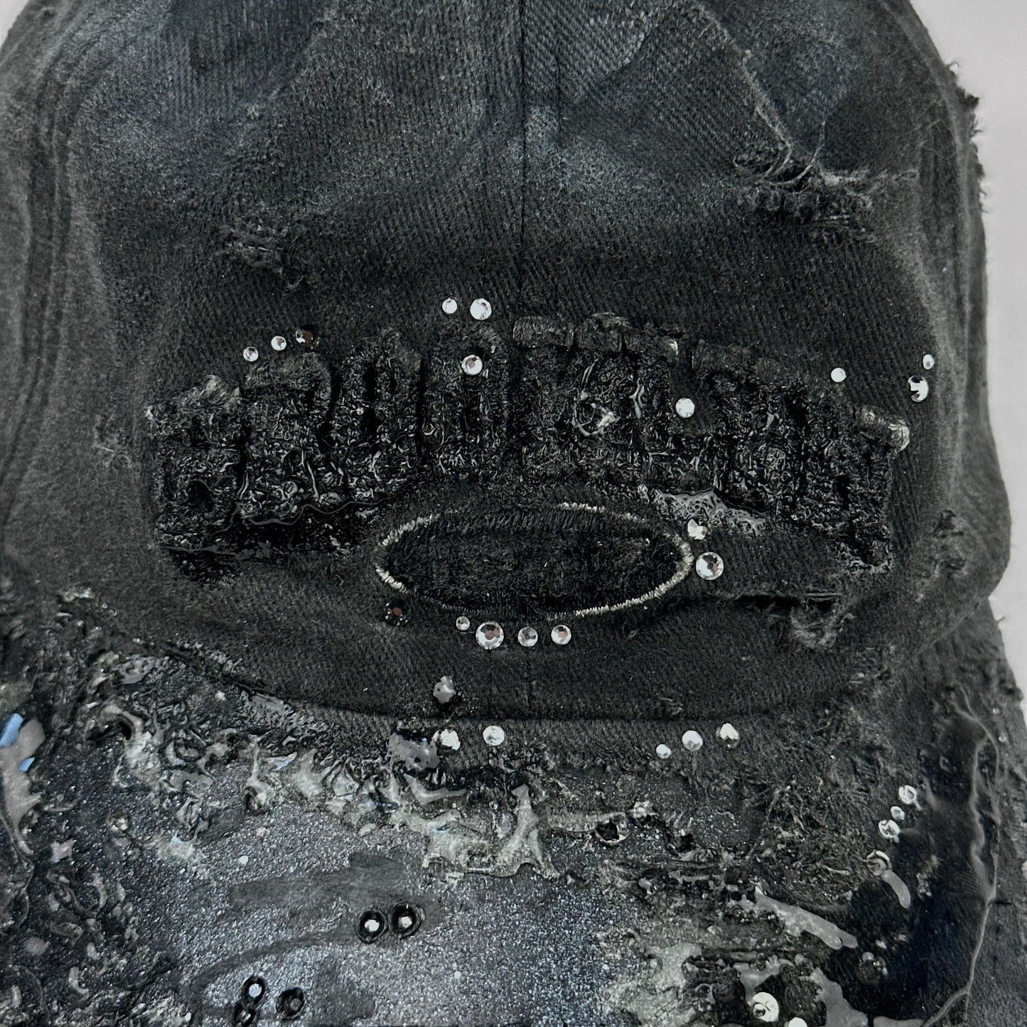 Logo detail on ASTROBOI* 'Alastair' black distressed resin hat with clear resin-encased Brooklyn logo at center front, silver rhinestone embellishments, and custom black resin detailing, handcrafted in NYC.
