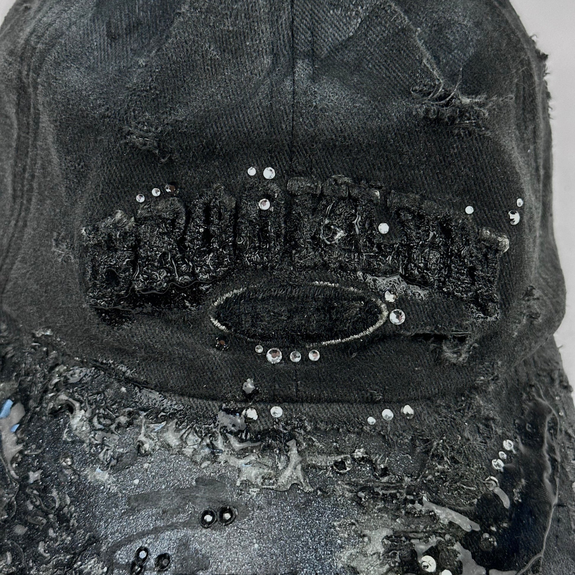 Logo detail on ASTROBOI* 'Alastair' black distressed resin hat with clear resin-encased Brooklyn logo at center front, silver rhinestone embellishments, and custom black resin detailing, handcrafted in NYC.