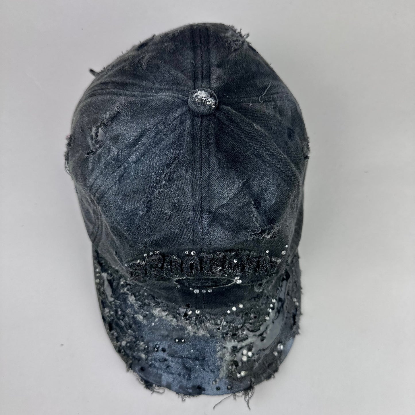 Top of ASTROBOI* 'Alastair' black distressed resin hat with clear resin-encased Brooklyn logo at center front, silver rhinestone embellishments, and custom black resin detailing, handcrafted in NYC.