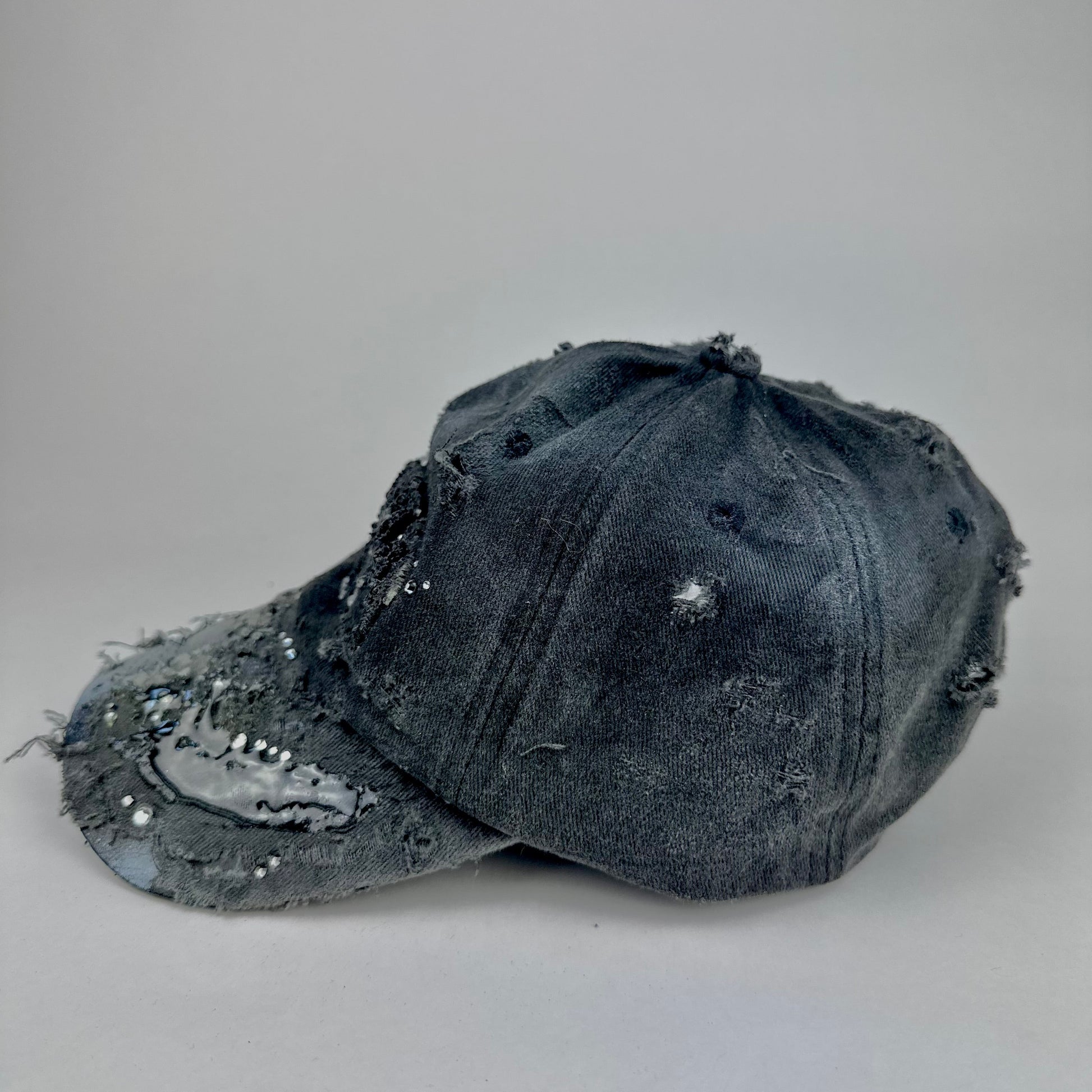 Left side of ASTROBOI* 'Alastair' black distressed resin hat with clear resin-encased Brooklyn logo at center front, silver rhinestone embellishments, and custom black resin detailing, handcrafted in NYC.