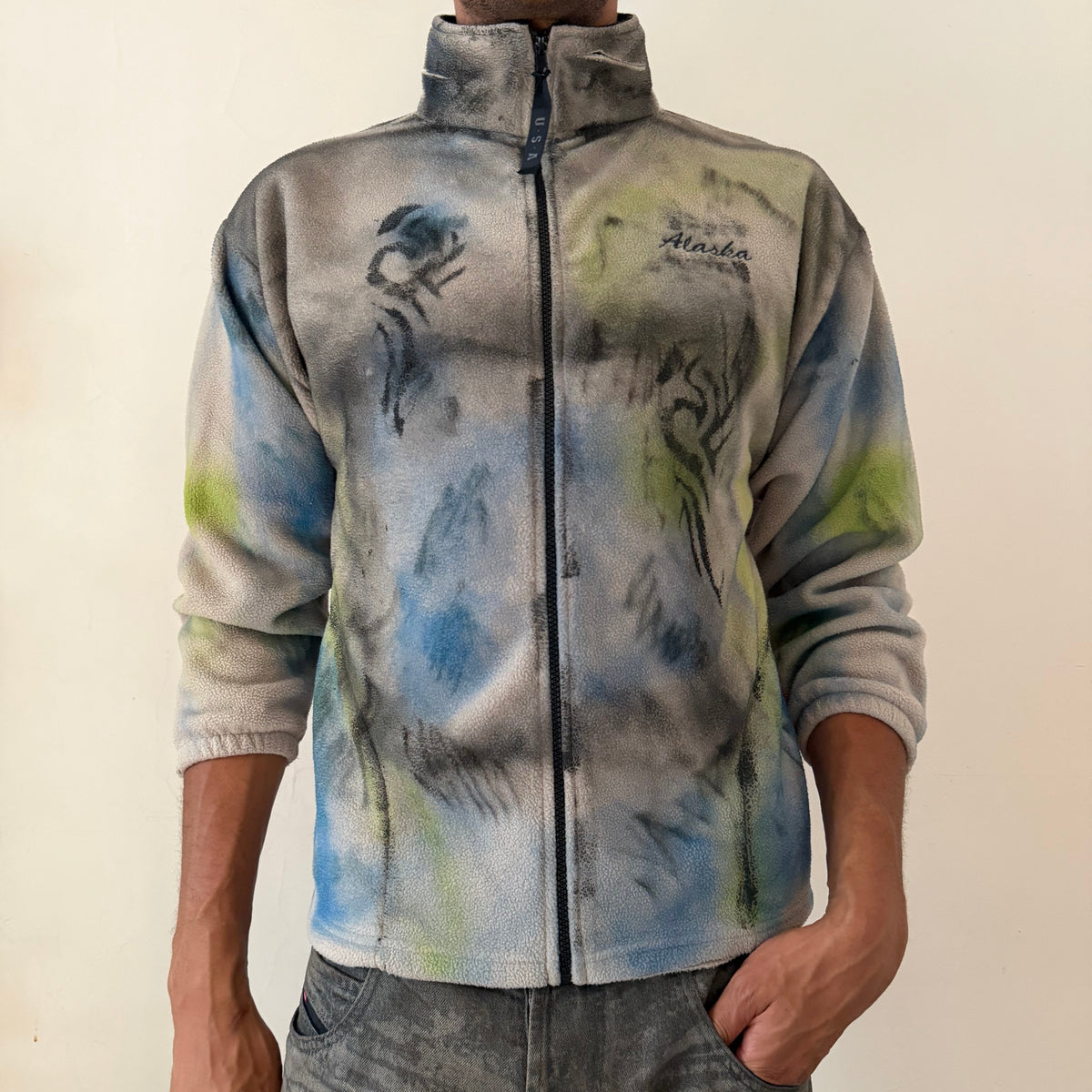 ASTROBOI* ‘Alaska’ Y2K tan fleece zip up sweatshirt with tattoo sketch doodle print, black flame design, multicolored abstract print, Alaska embroidery at right chest, and USA zipper pull tab, front view.
