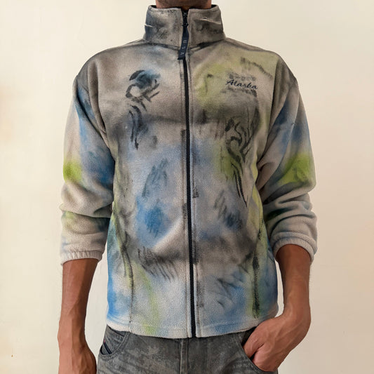 ASTROBOI* ‘Alaska’ Y2K tan fleece zip up sweatshirt with tattoo sketch doodle print, black flame design, multicolored abstract print, Alaska embroidery at right chest, and USA zipper pull tab, front view.