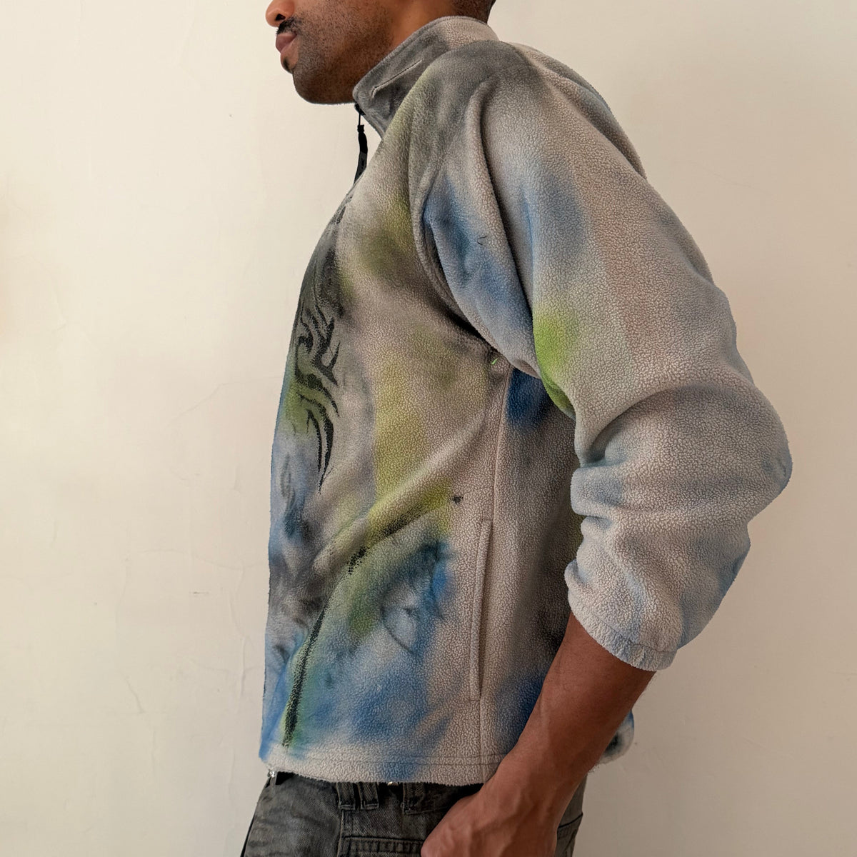 Left side detail of ASTROBOI* ‘Alaska’ showing multicolored abstract print, black flame design, and hip pocket detail on boxy tan fleece zip up.