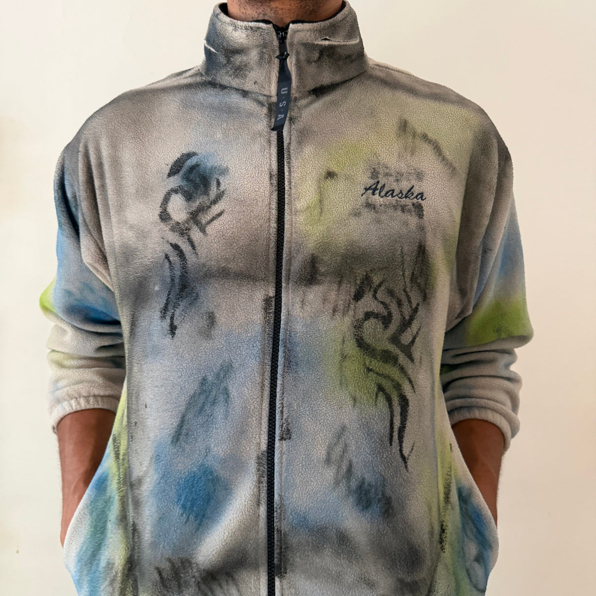 Close-up of ASTROBOI* ‘Alaska’ showing tattoo sketch doodle print, black flame design, and multicolored green, blue, and black abstract print on tan fleece fabric.