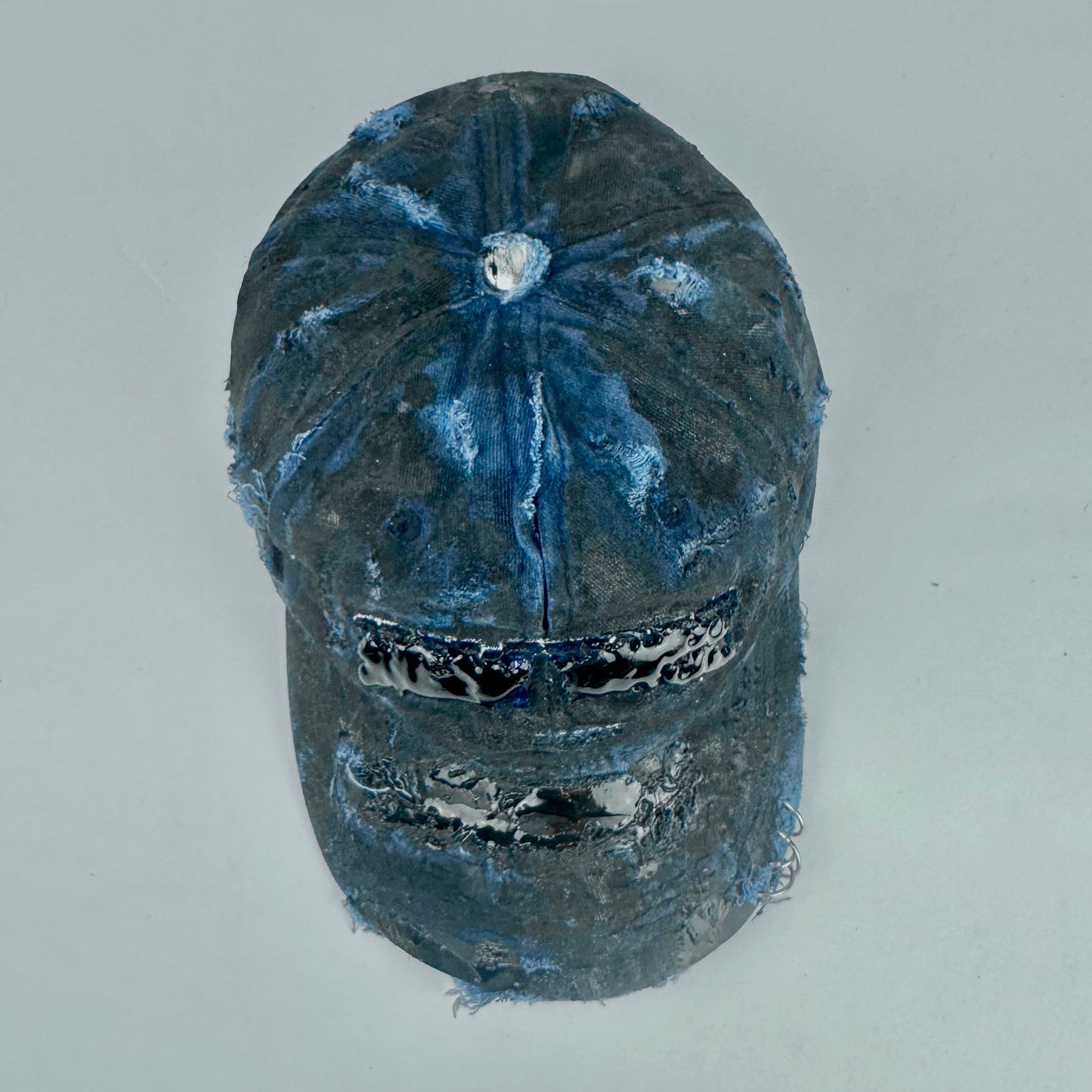 Top of ASTROBOI* 'Feeling Blue' distressed blue resin-coated hat with hand-painted black shading, metal piercings on the right front, and New York embroidery, handmade in NYC.