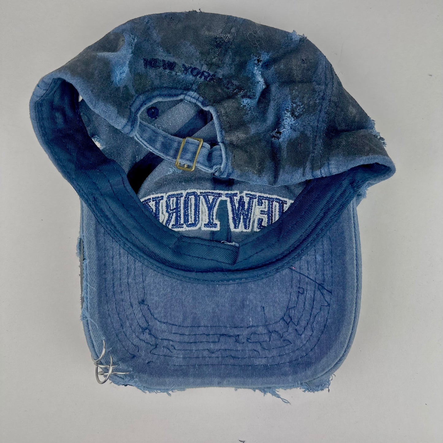Back of ASTROBOI* 'Feeling Blue' distressed blue resin-coated hat with hand-painted black shading, metal piercings on the right front, and New York embroidery, handmade in NYC.