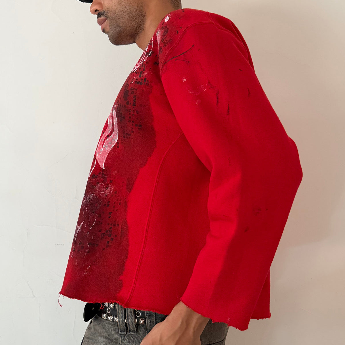 Left side detail of ASTROBOI* x Russell ‘Red Wave’ showing washed out digital camo and white Y2K flame winged design with raw hemline on red sweatshirt.