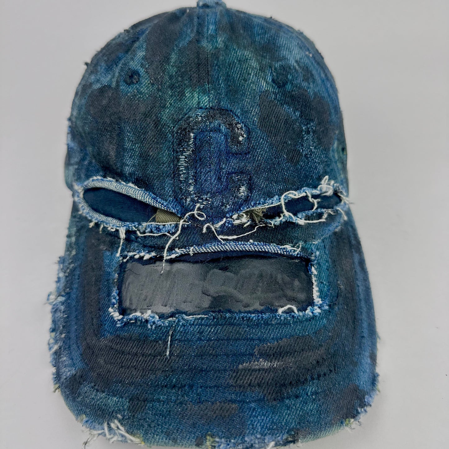 Front of ASTROBOI* 'C' deconstructed black and blue faded denim hat with hand-painted blue-green shading, raw crown cut-outs, and embossed C logo at center front, customized in NYC.