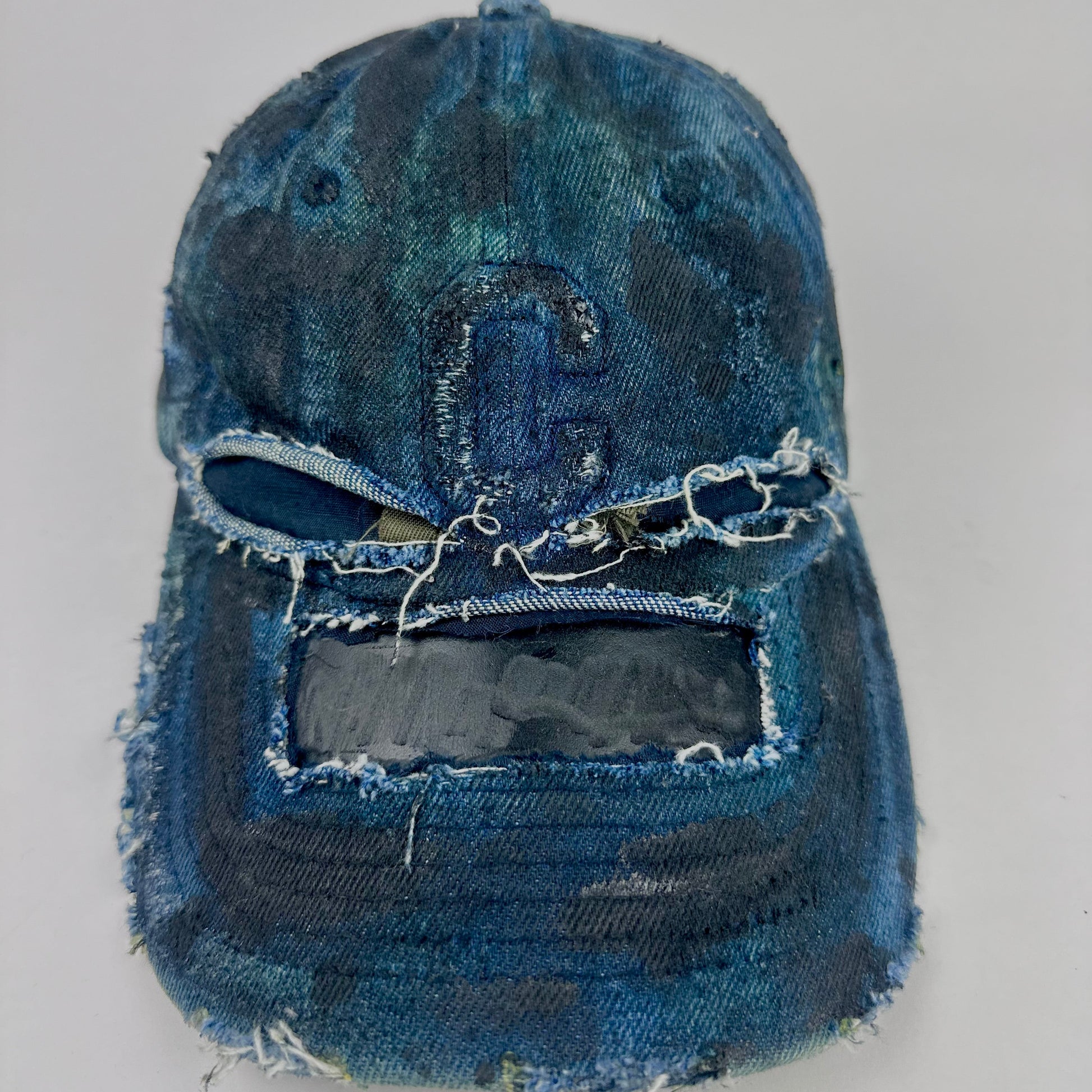 Front of ASTROBOI* 'C' deconstructed black and blue faded denim hat with hand-painted blue-green shading, raw crown cut-outs, and embossed C logo at center front, customized in NYC.