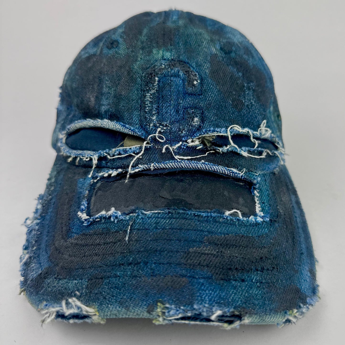 Frontal overview of ASTROBOI* 'C' deconstructed black and blue faded denim hat with hand-painted blue-green shading, raw crown cut-outs, and embossed C logo at center front, customized in NYC.
