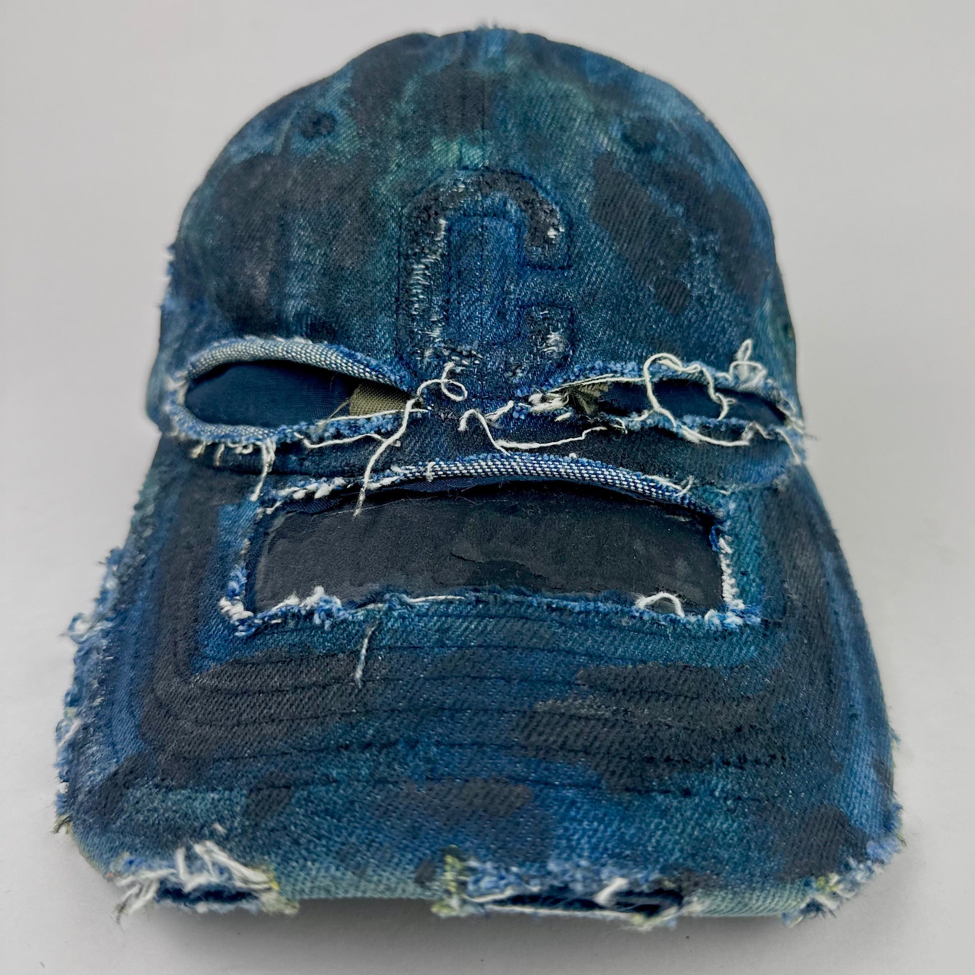 Frontal overview of ASTROBOI* 'C' deconstructed black and blue faded denim hat with hand-painted blue-green shading, raw crown cut-outs, and embossed C logo at center front, customized in NYC.