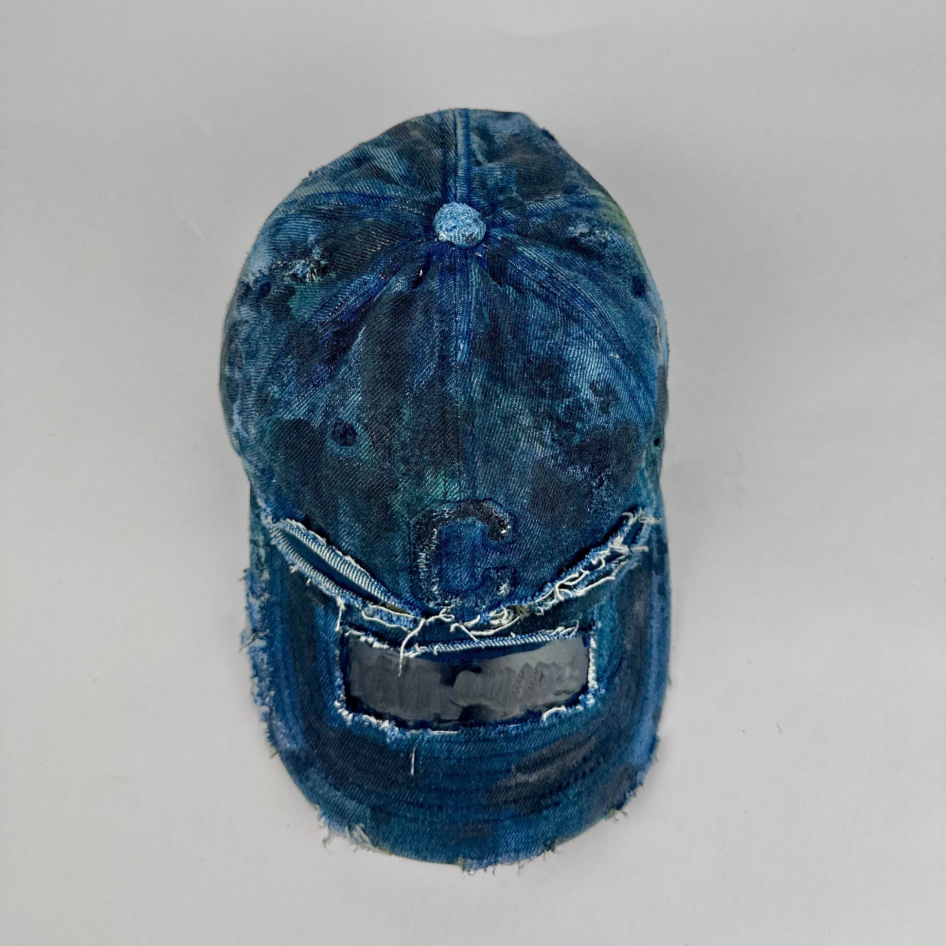 Top of ASTROBOI* 'C' deconstructed black and blue faded denim hat with hand-painted blue-green shading, raw crown cut-outs, and embossed C logo at center front, customized in NYC.