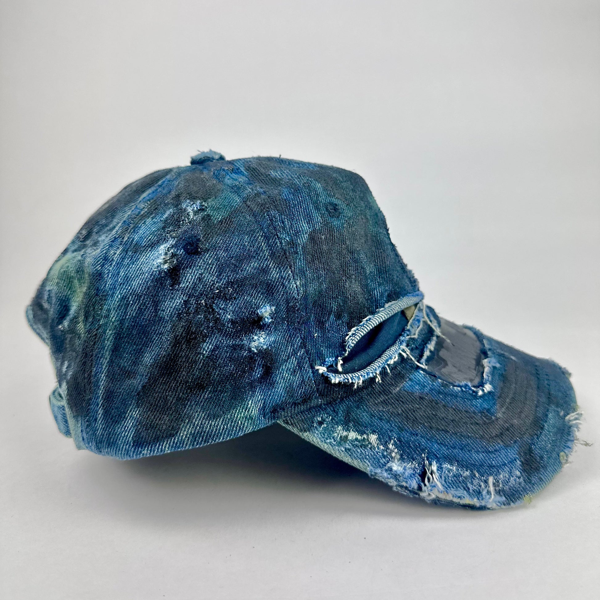 Right side of ASTROBOI* 'C' deconstructed black and blue faded denim hat with hand-painted blue-green shading, raw crown cut-outs, and embossed C logo at center front, customized in NYC.