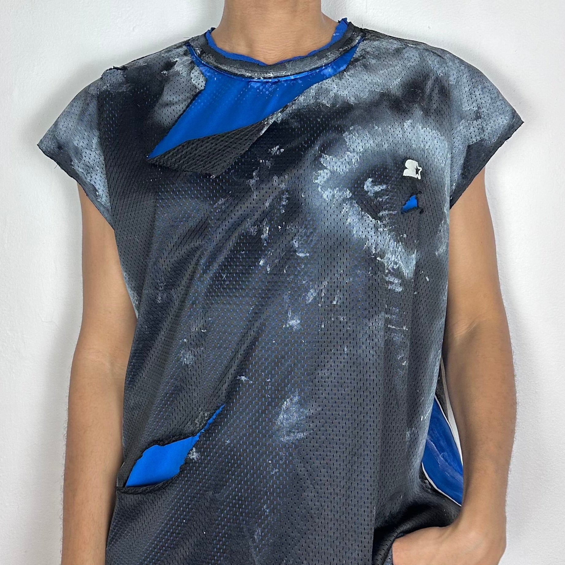 Close-up of ASTROBOI* x Starter mesh tank showing ripped black mesh detail, blue interior layer reveal, and scattered white paint pattern on fabric.