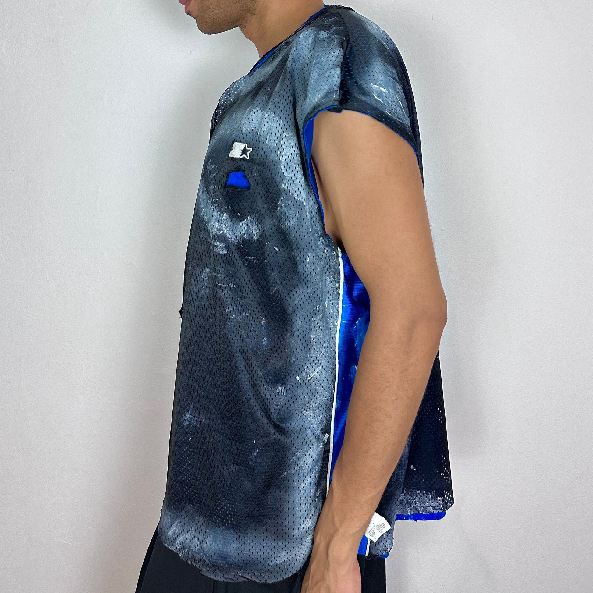 Left side detail of ASTROBOI* x Starter mesh tank showing artfully ripped mesh construction, blue interior reveal, and scattered white paint pattern.