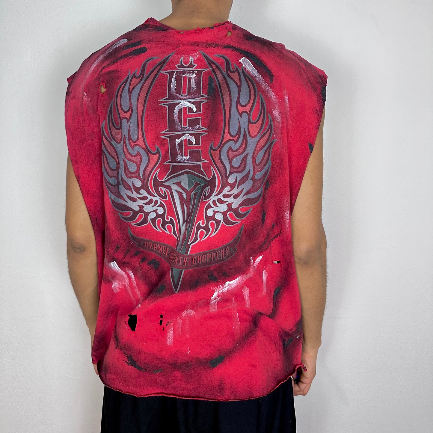 ASTROBOI* Y2K Orange County Choppers red muscle tank top, rear view showing OCC branding, branded sword graphic, airbrush detailing, and paint splatter, worn by male model.