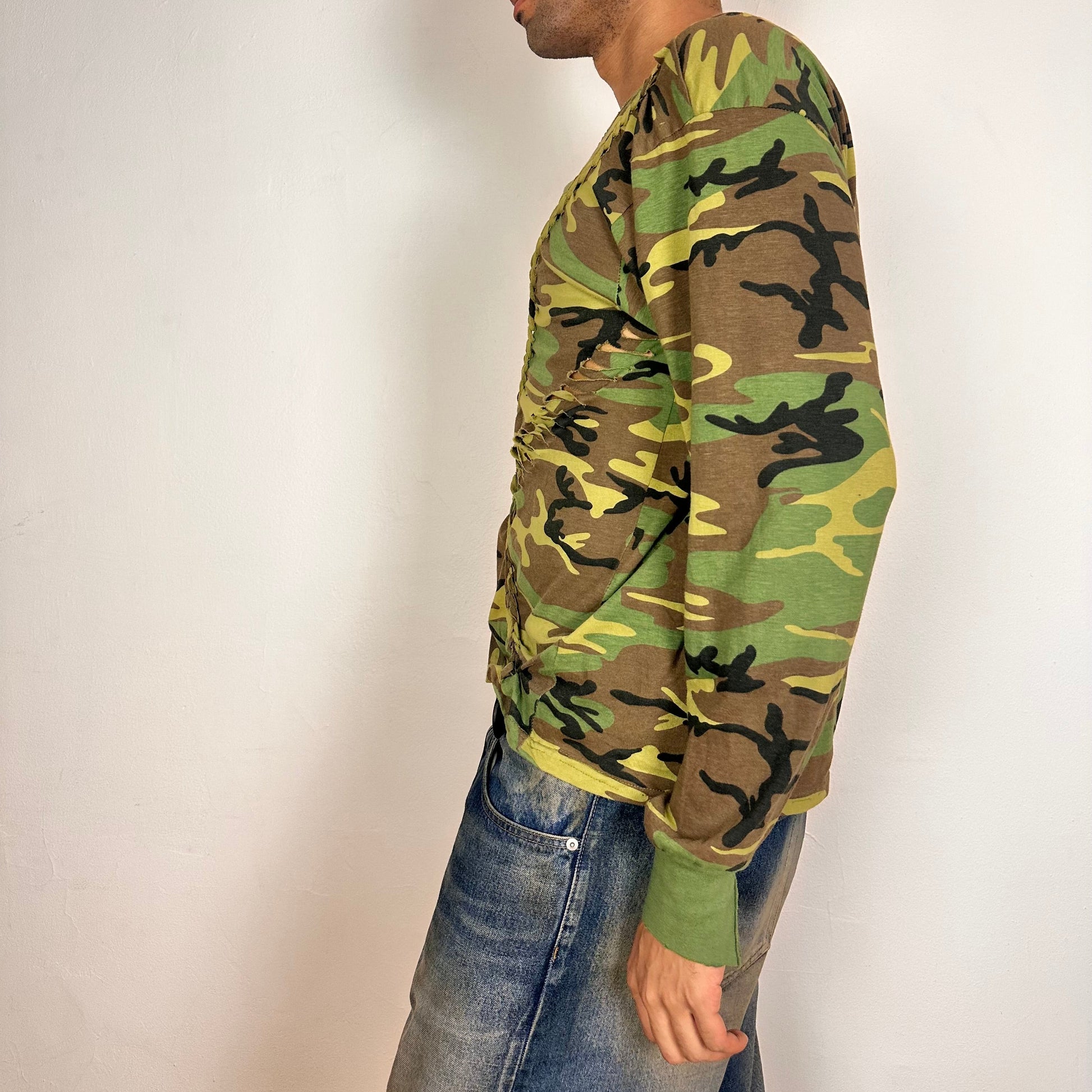 Left side of ASTROBOI* green camouflage T-shirt with braided detailing, tonal rhinestone collar, raw hem, and loose fit, handmade in NYC.