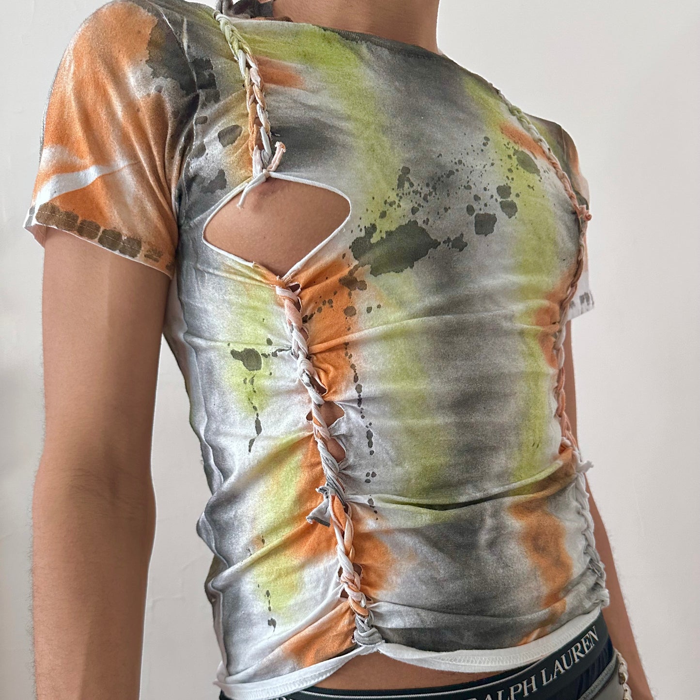 Close-up of ASTROBOI* x Gildan 'Orange Haze' showing hand-painted black, gray, and orange abstract design and subtle braid detail on white cotton fabric.