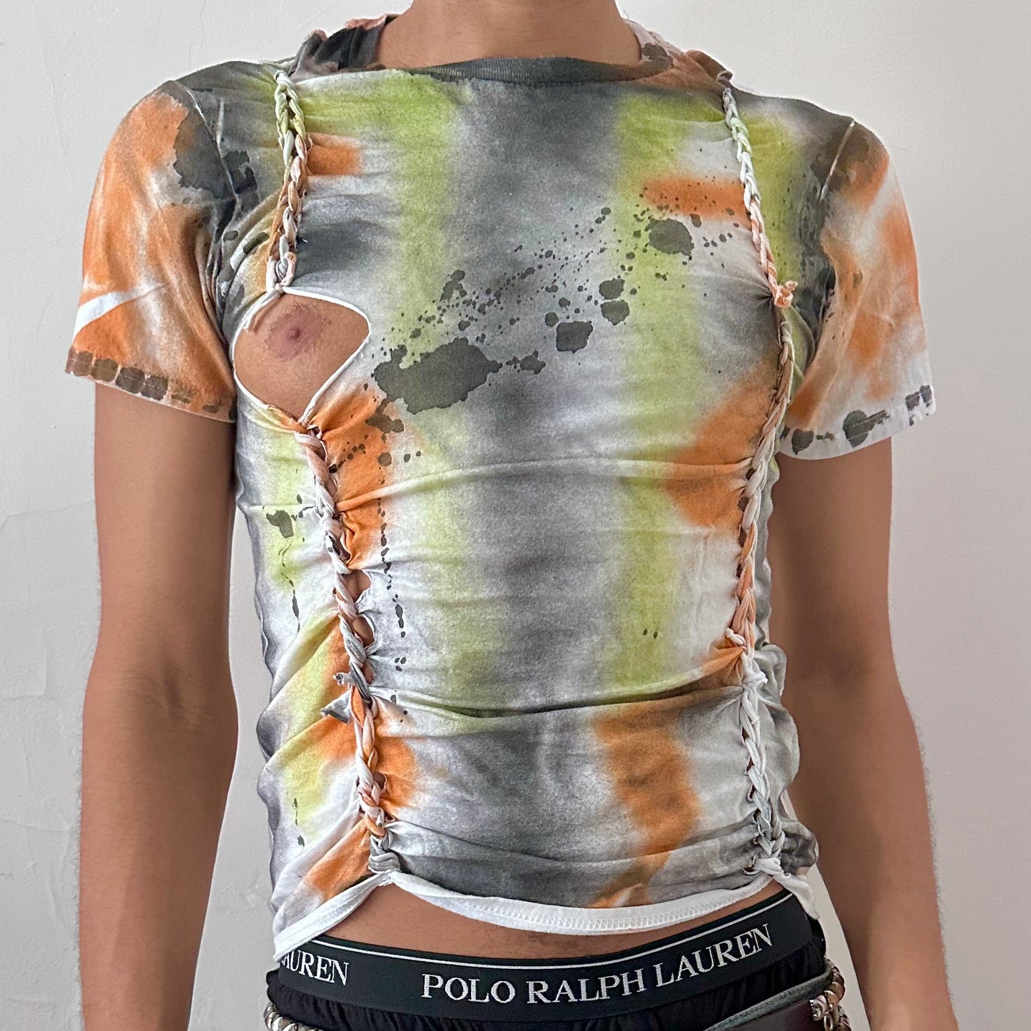 Close-up of ASTROBOI* x Gildan 'Orange Haze' showing hand-painted black, gray, and orange abstract design and subtle braid detail on white cotton fabric.